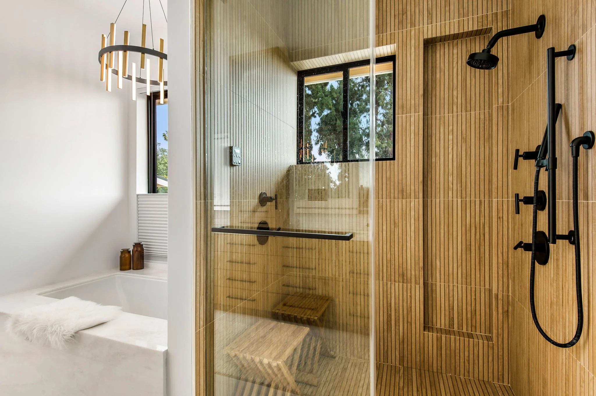 Modern bathroom with a white marble tub, glass shower enclosure, wood-paneled walls, and black fixtures.