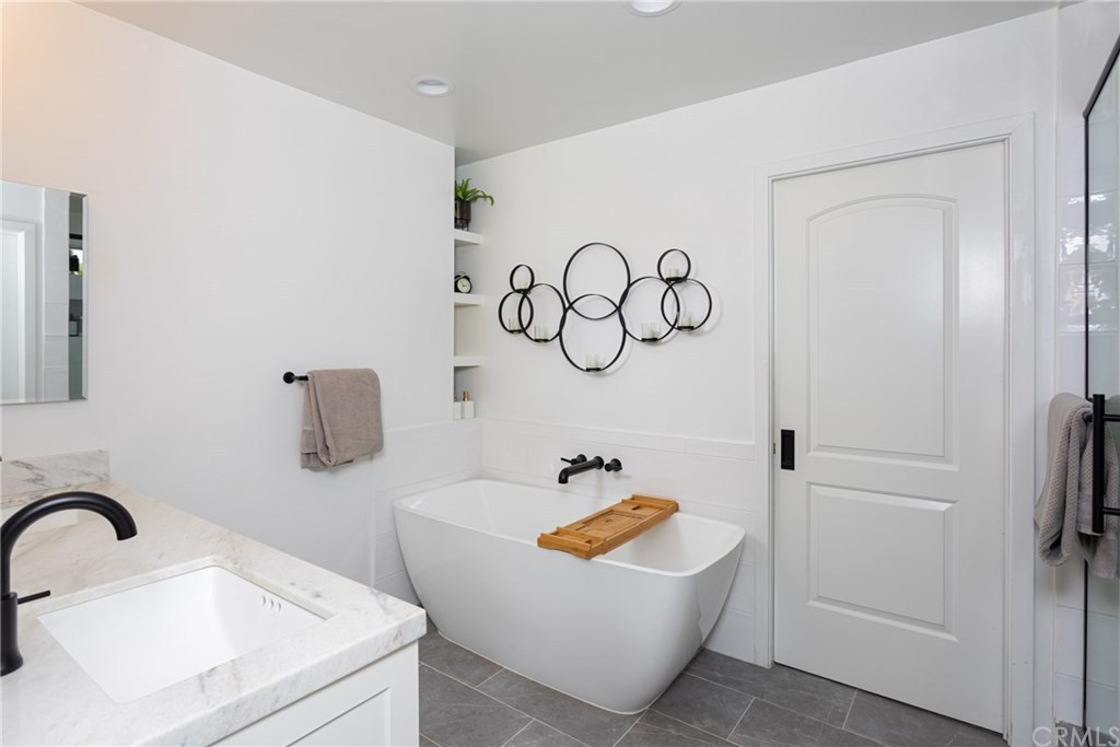 Modern white bathroom with a freestanding tub, marble vanity, and black fixtures.