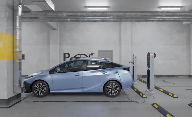 A light blue electric car charging in a concrete parking garage with an EV charging symbol on the wall.