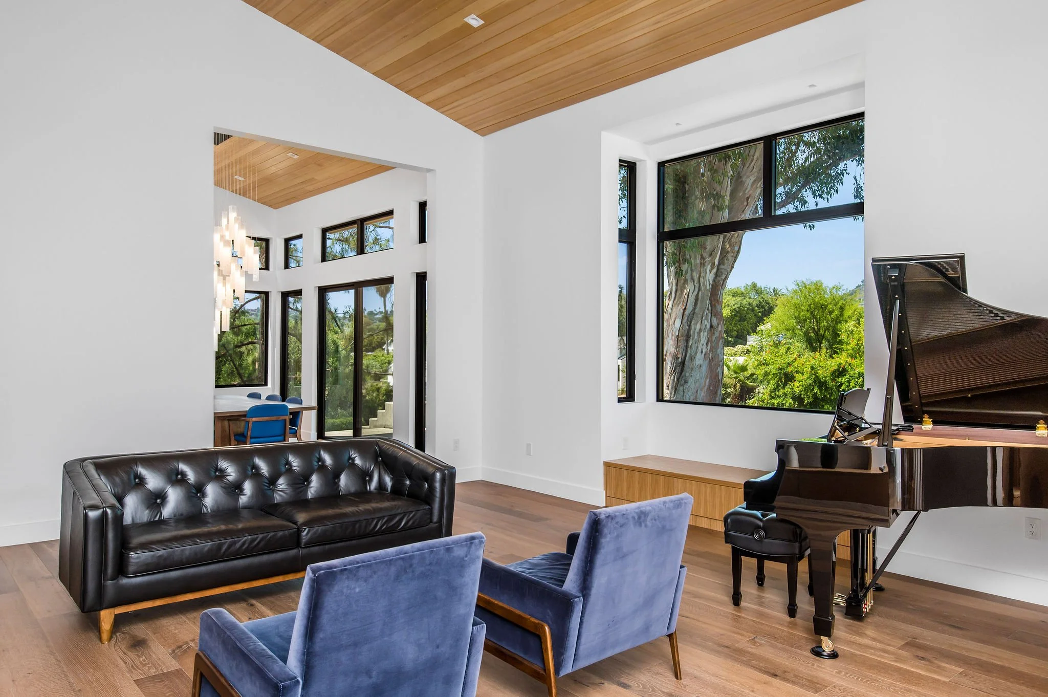 Modern living room with a black leather sofa, two blue velvet chairs, and a grand piano.