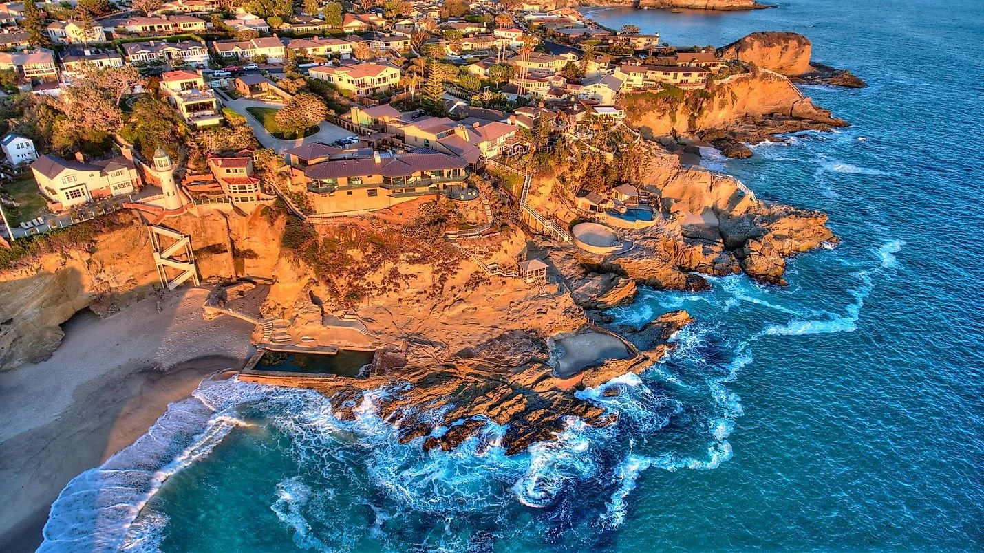 Aerial view of cliffside homes and tidal pools along the Laguna Beach coastline at sunset.