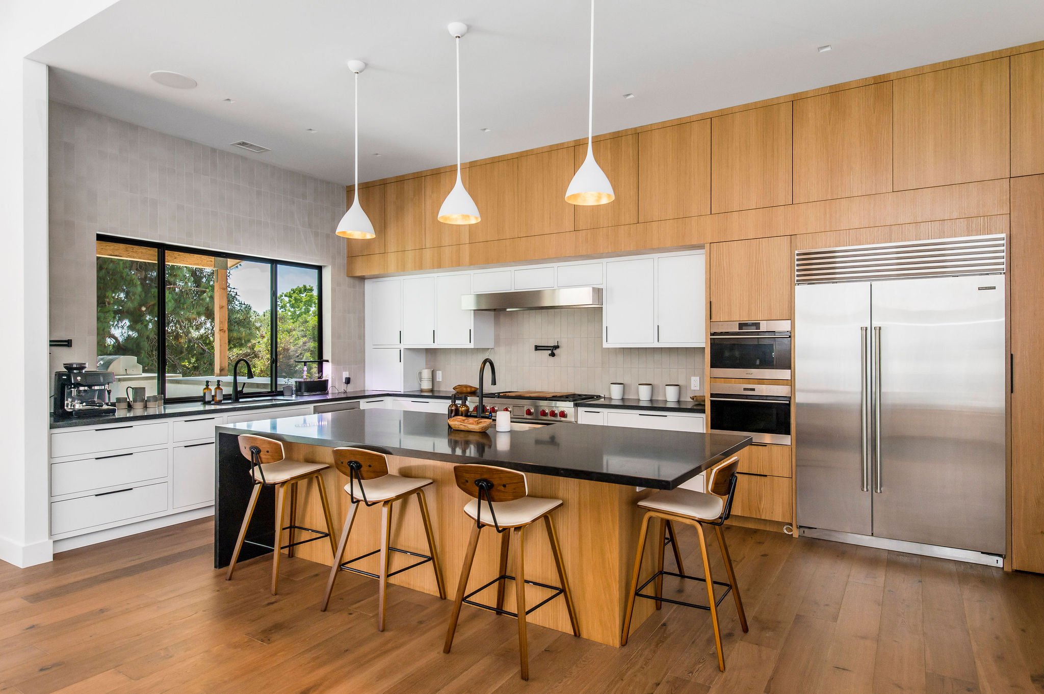 Modern kitchen with light wood and white cabinets, black countertops, stainless steel appliances, and a large island.