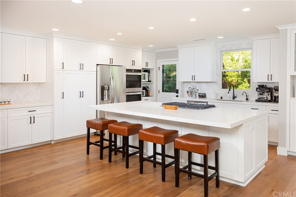 Modern kitchen with white cabinets, stainless steel appliances, a large island with four leather stools, and hardwood floors.