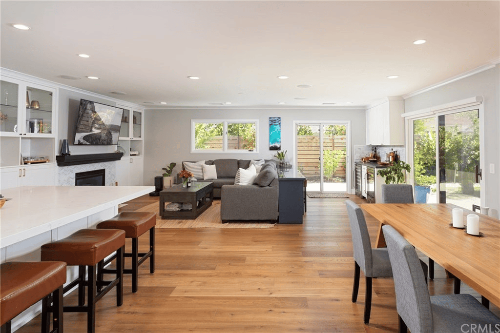 Open-concept living room and kitchen with hardwood floors, a gray sectional, and a light wood dining table.