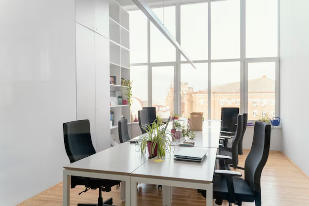 Modern office space with a long white table, black chairs, plants, and a large window overlooking a city.