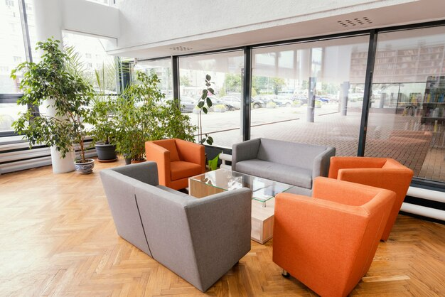 Lobby with gray and orange seating, glass tables, potted plants, and large windows looking out onto a parking lot.