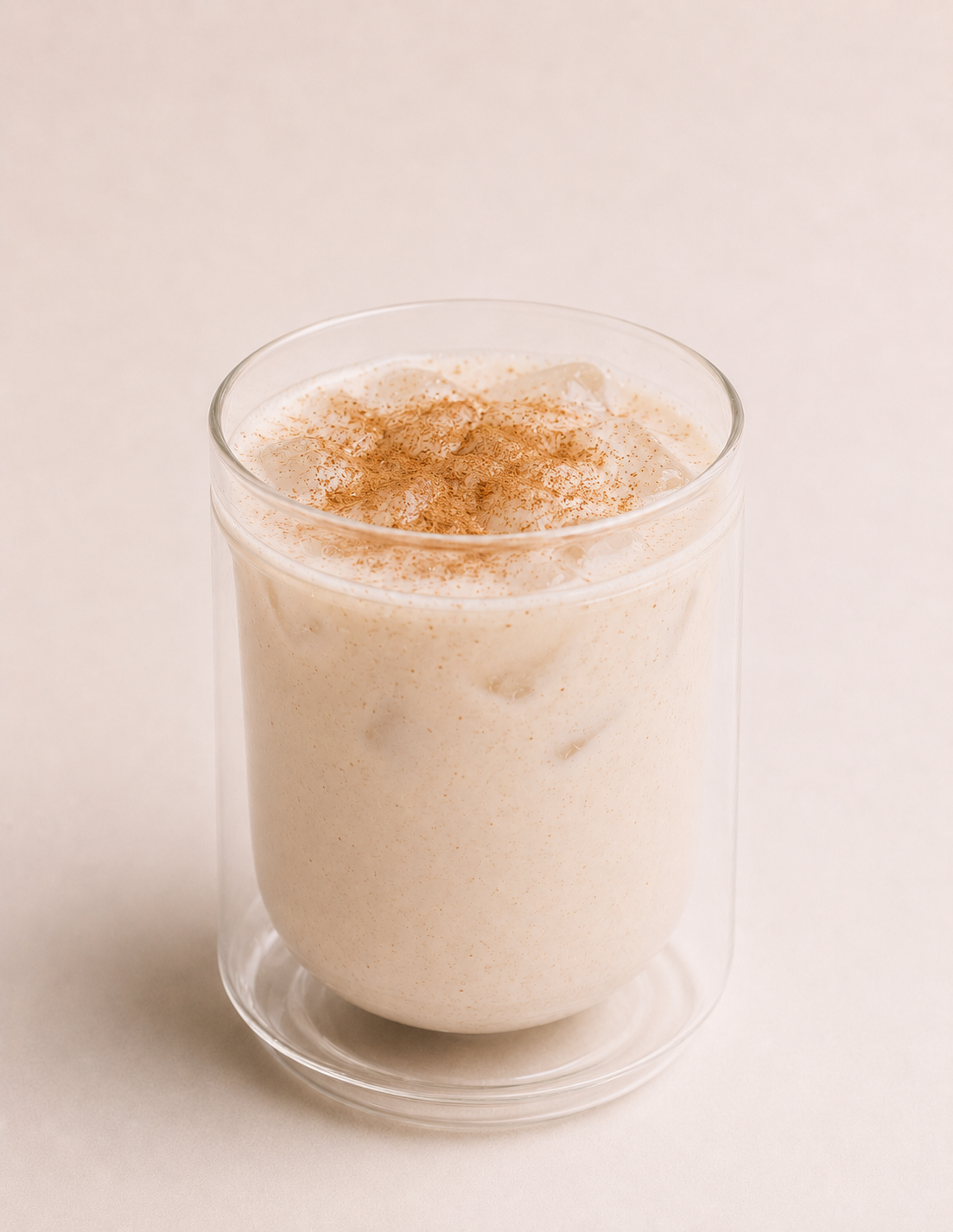 Glass of iced vanilla latte topped with cinnamon powder on a white background.