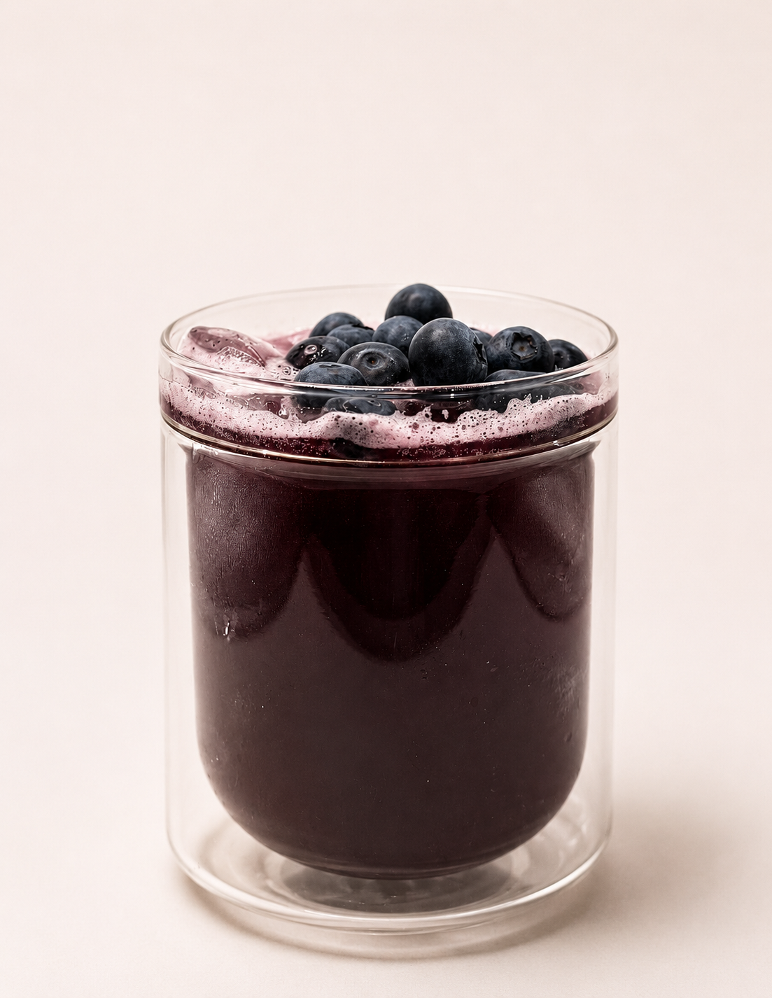 A glass of blueberry juice topped with fresh blueberries and ice cubes.