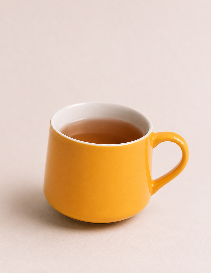 Yellow ceramic mug filled with tea on a light beige background.