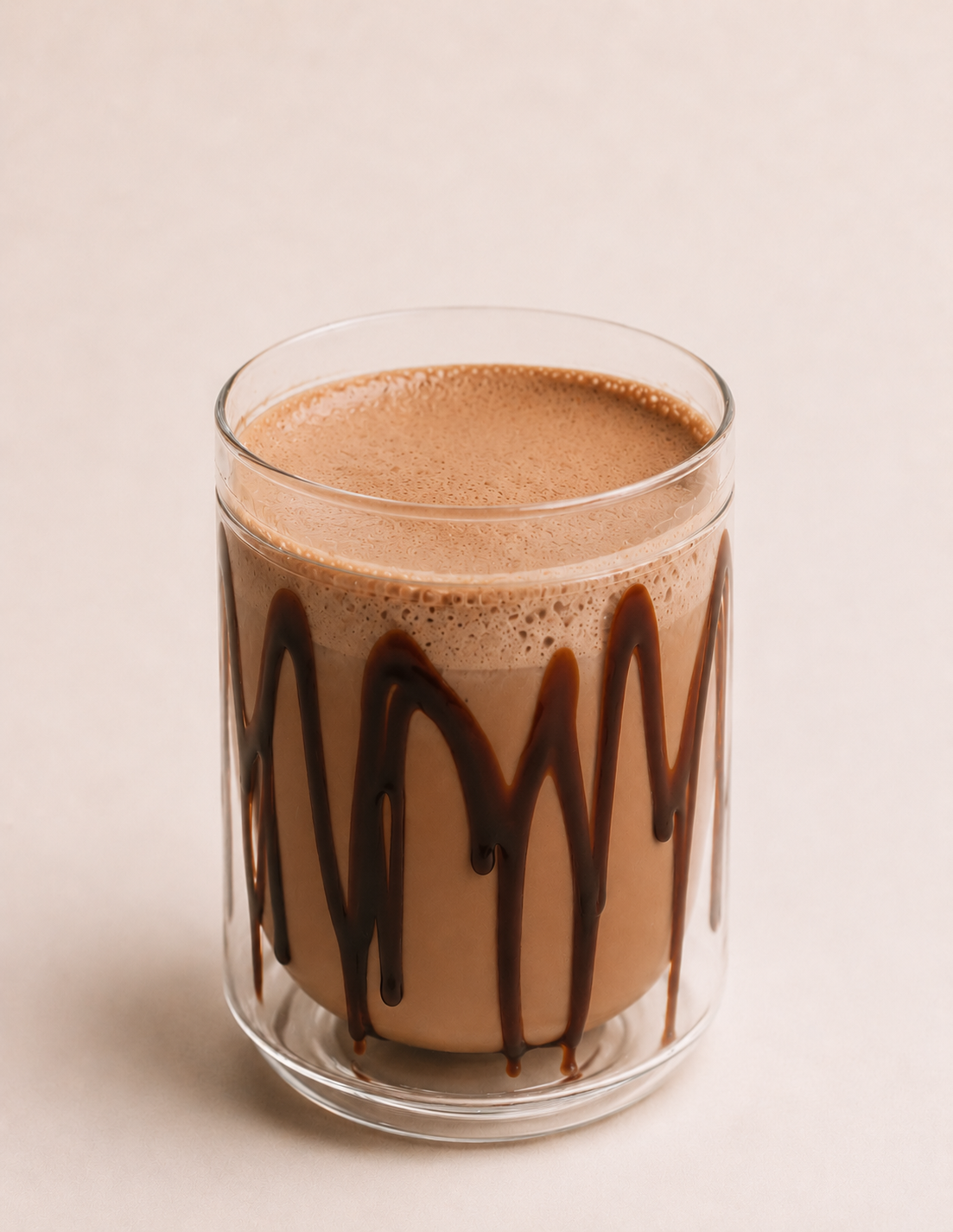 A glass of chocolate milk with chocolate drizzle on the outside glass.