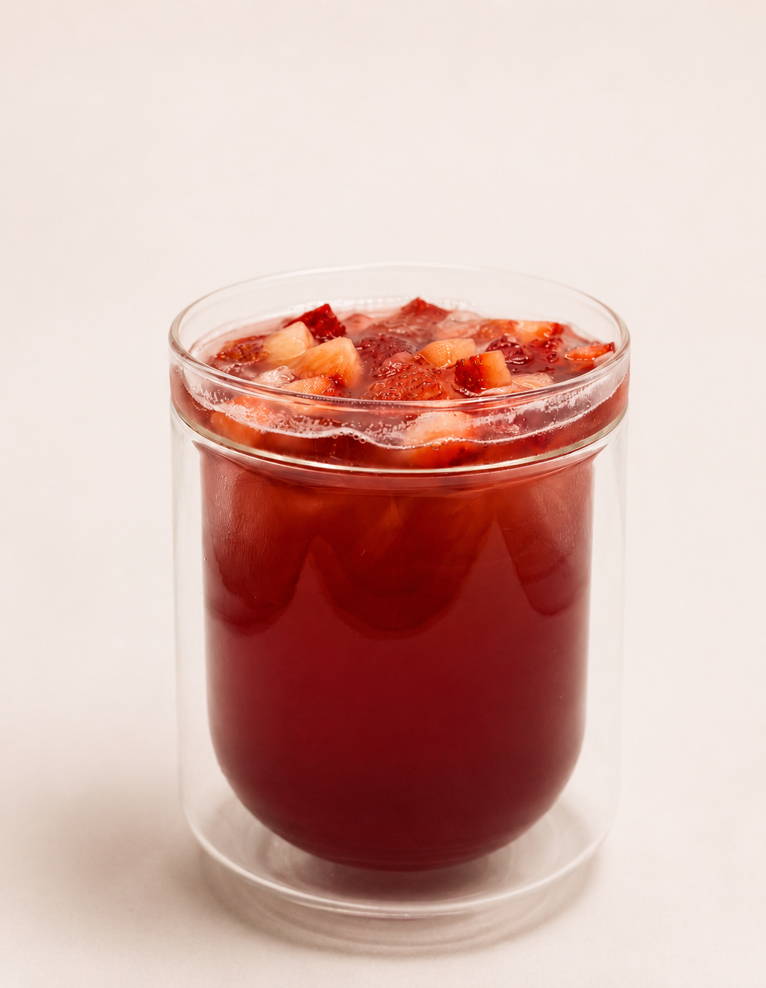 A clear glass filled with red strawberry beverage topped with chopped strawberries.