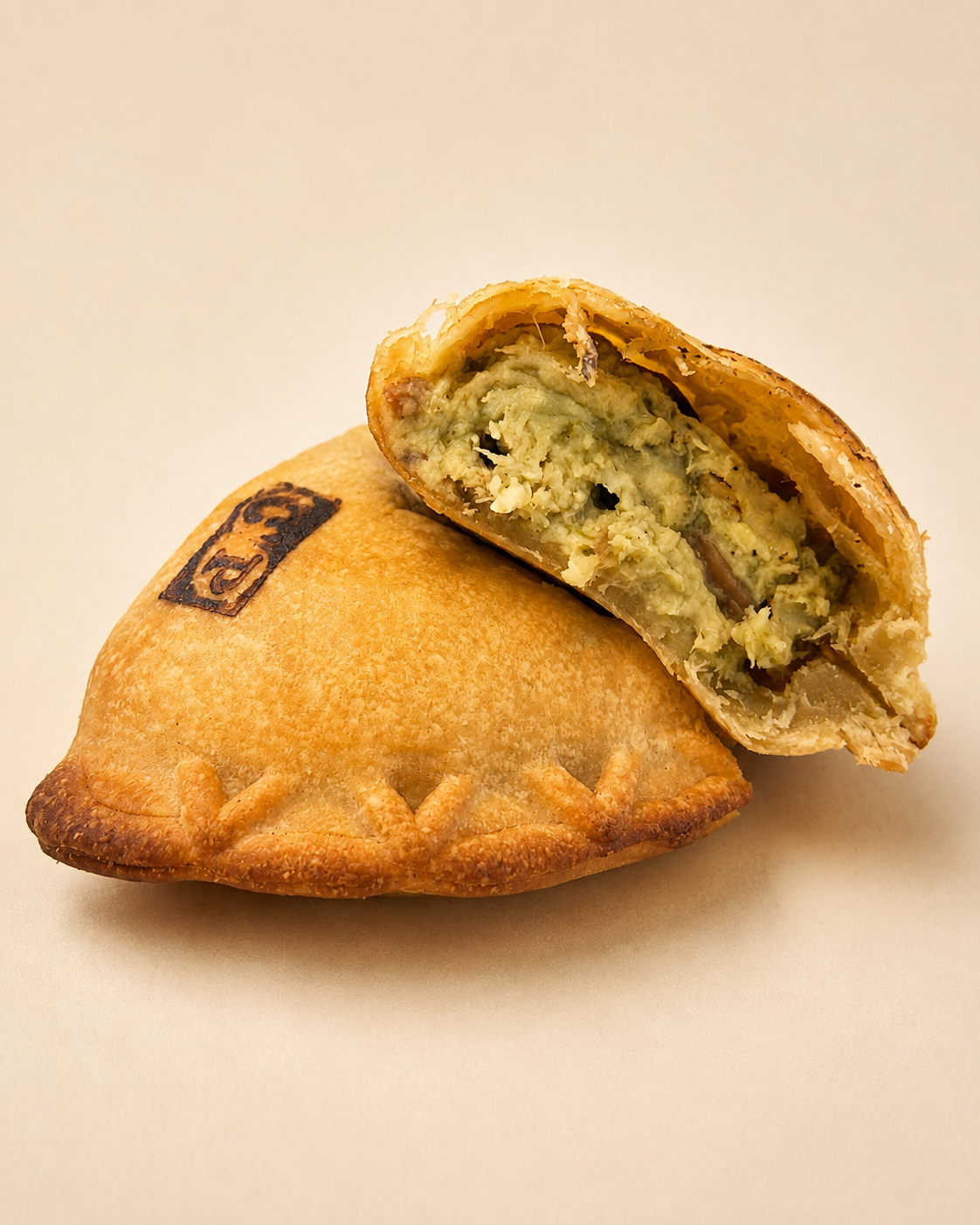 A baked hand pie with a decorative edge, partially cut open to reveal a filling of chicken and vegetables, resting on black and white printed paper.