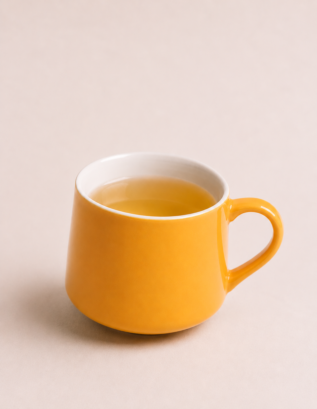 Yellow ceramic mug filled with tea on a light beige surface against a plain beige background.