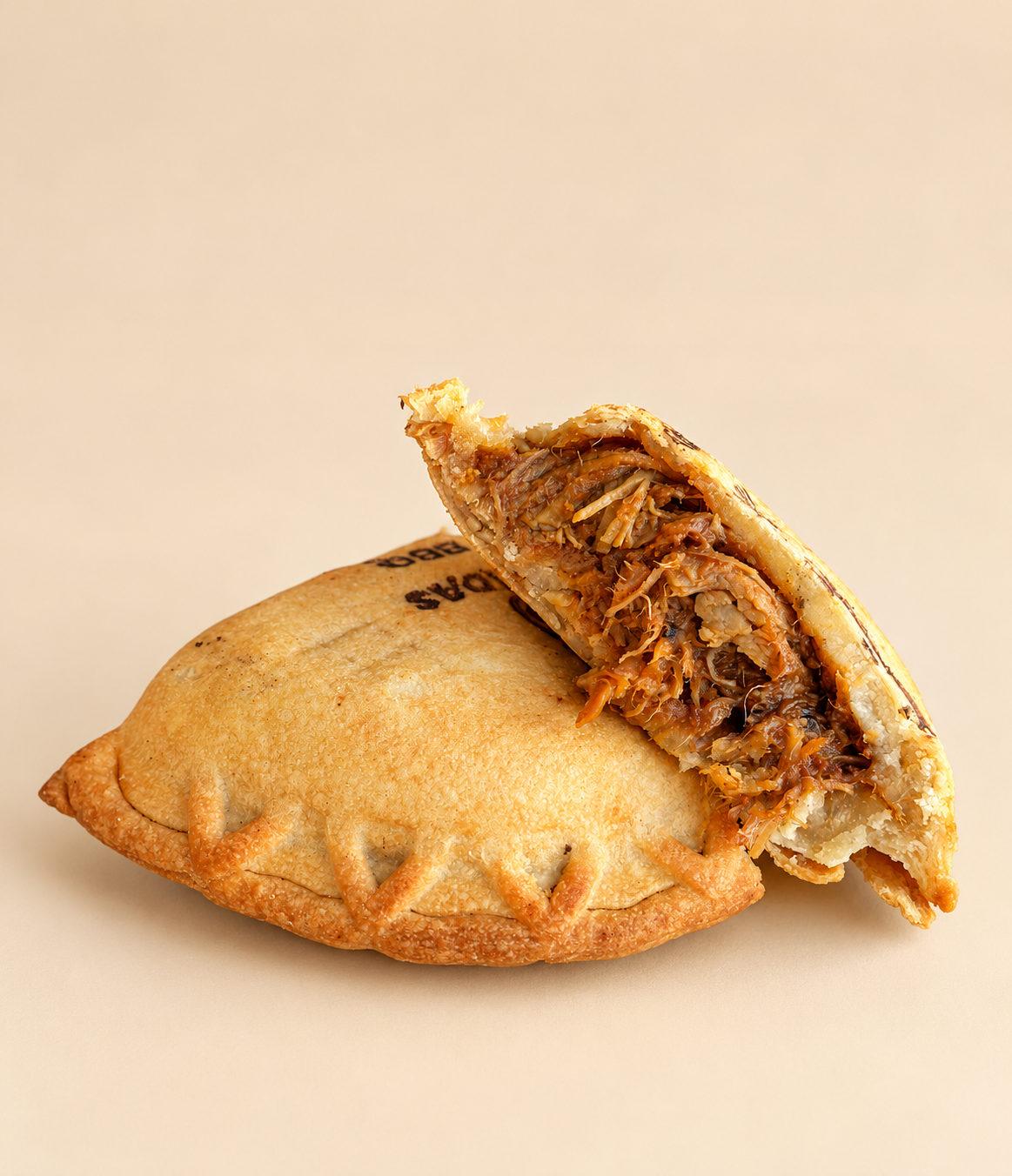 A cut empanada on a patterned paper background. The filling is visible, showing shredded meat.