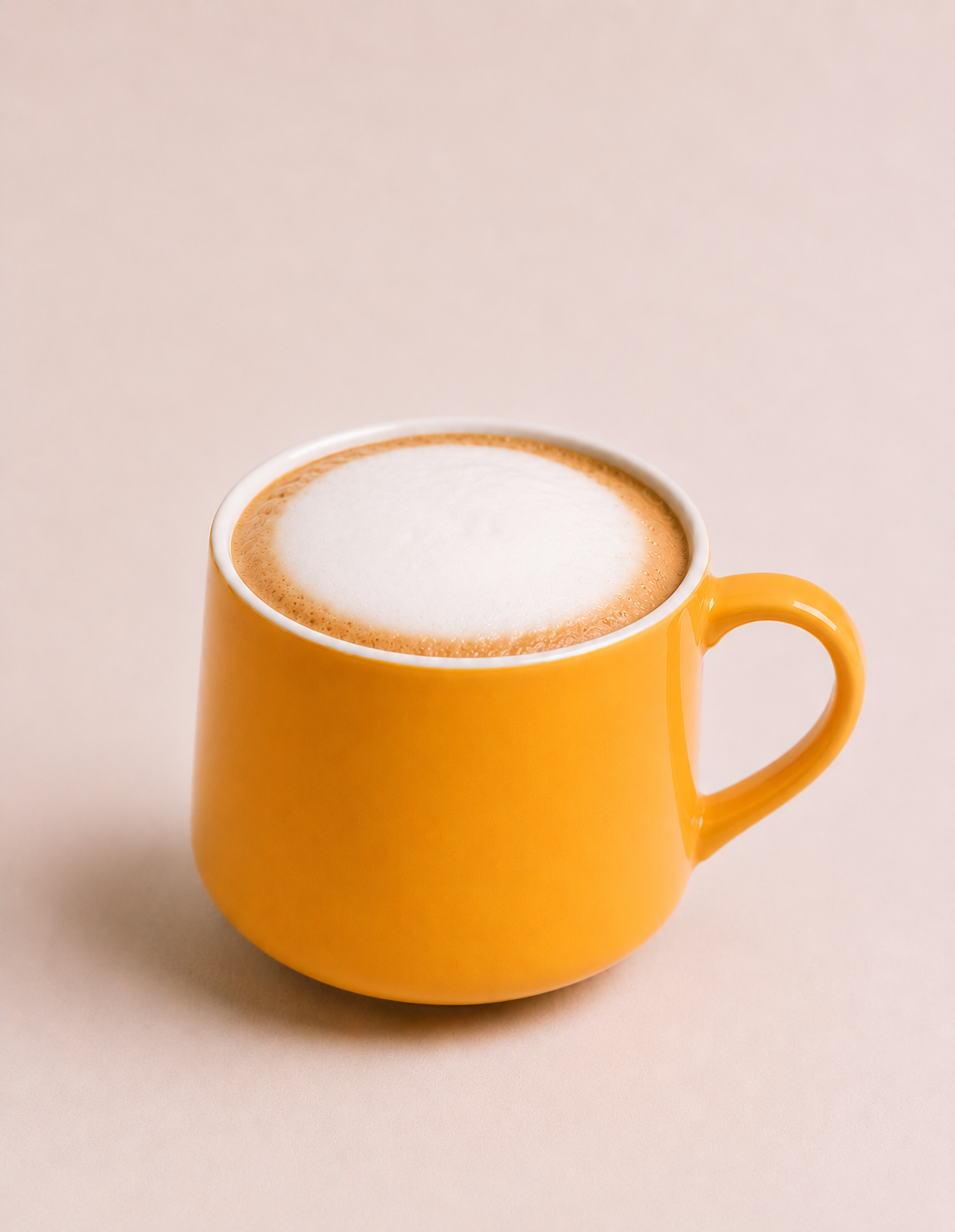 Yellow mug filled with frothy cappuccino against a neutral background.