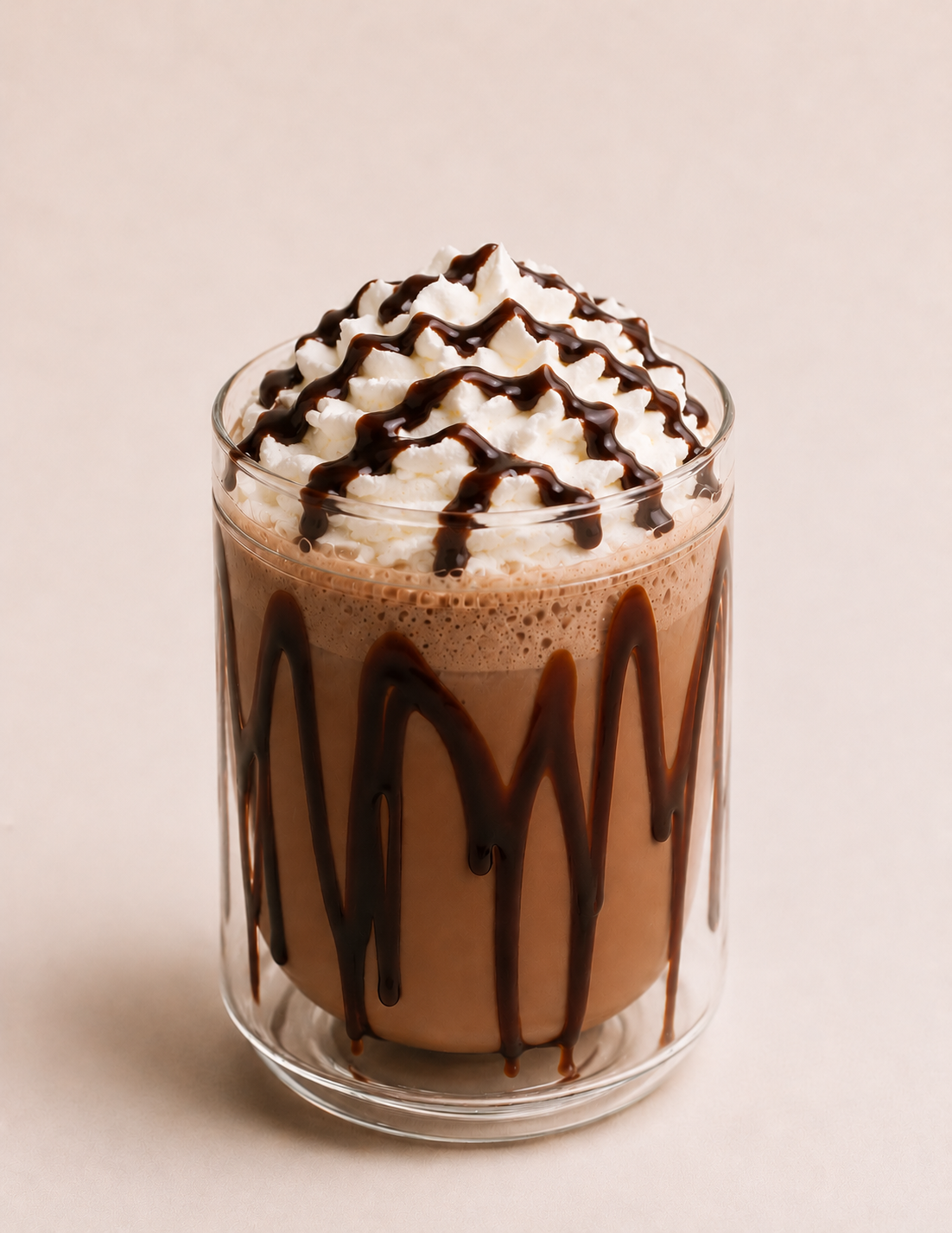 A tall glass of chocolate milkshake topped with whipped cream and drizzled with chocolate syrup, with similar syrup on the outside of the glass.