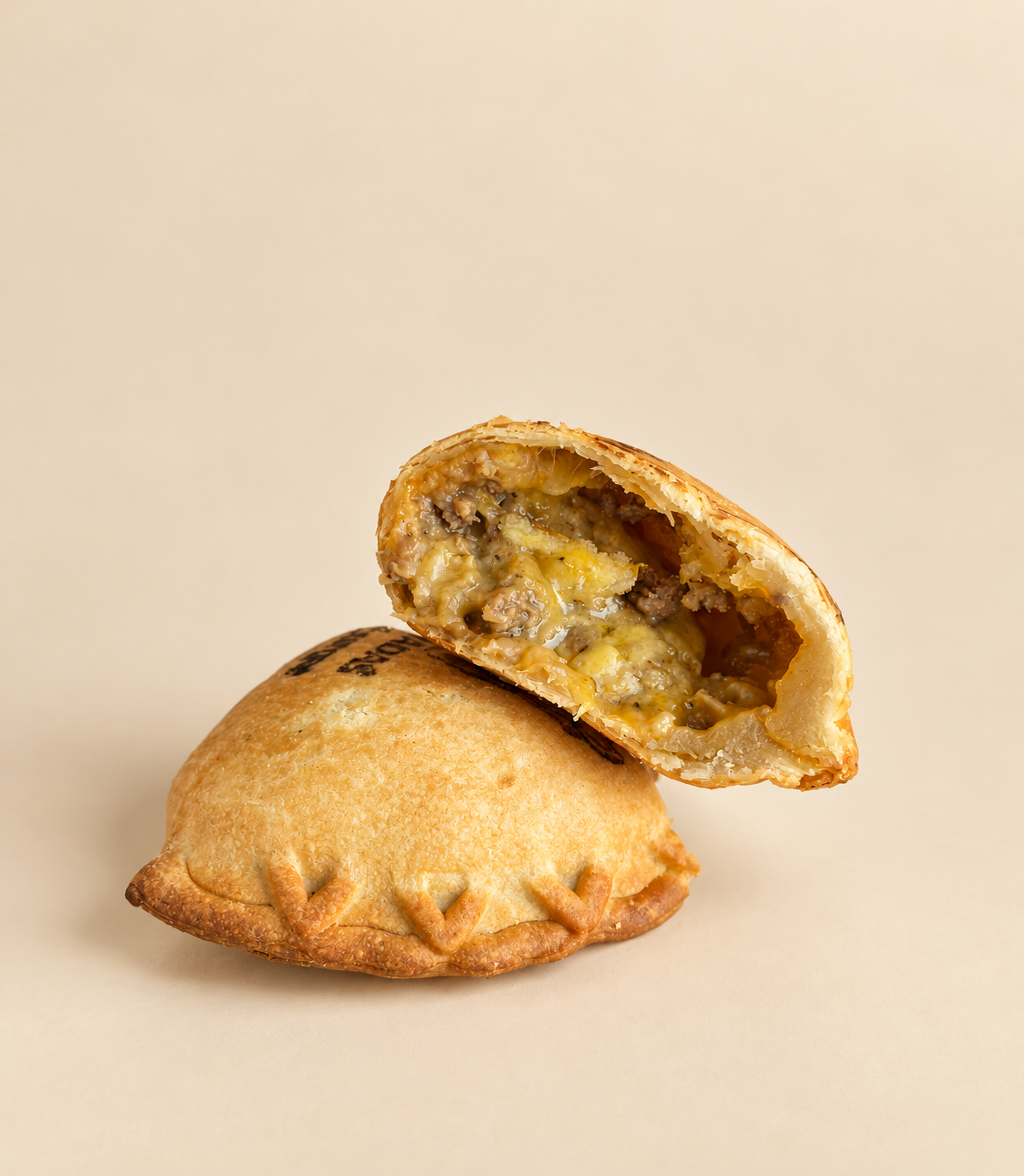 Two baked ingredients: one of a golden-brown savory meat pie with flaky crust, partially bitten to reveal a filling of seasoned ground meat and vegetables, placed on black and white printed paper
