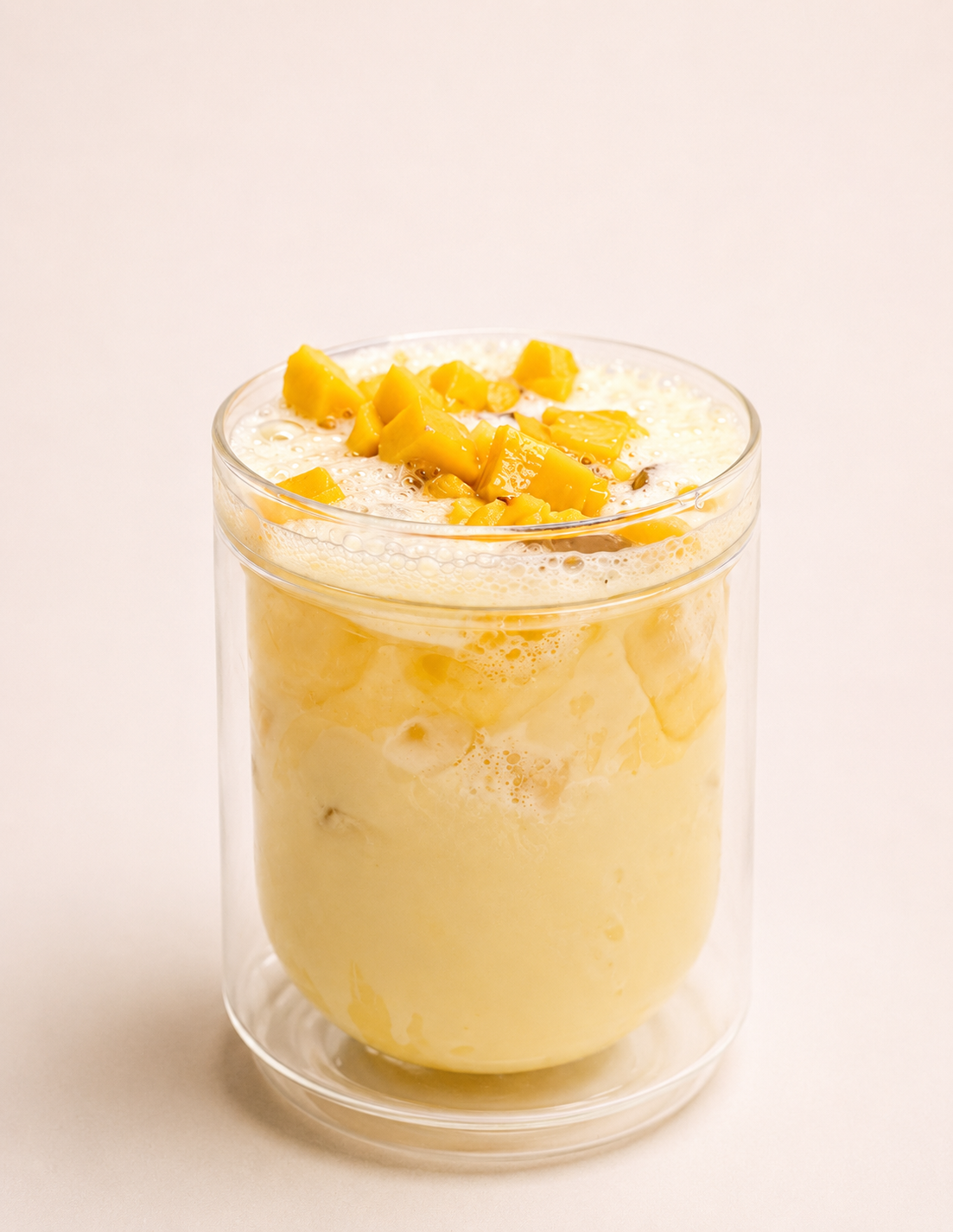 Mango smoothie in a clear glass with mango chunks on top.