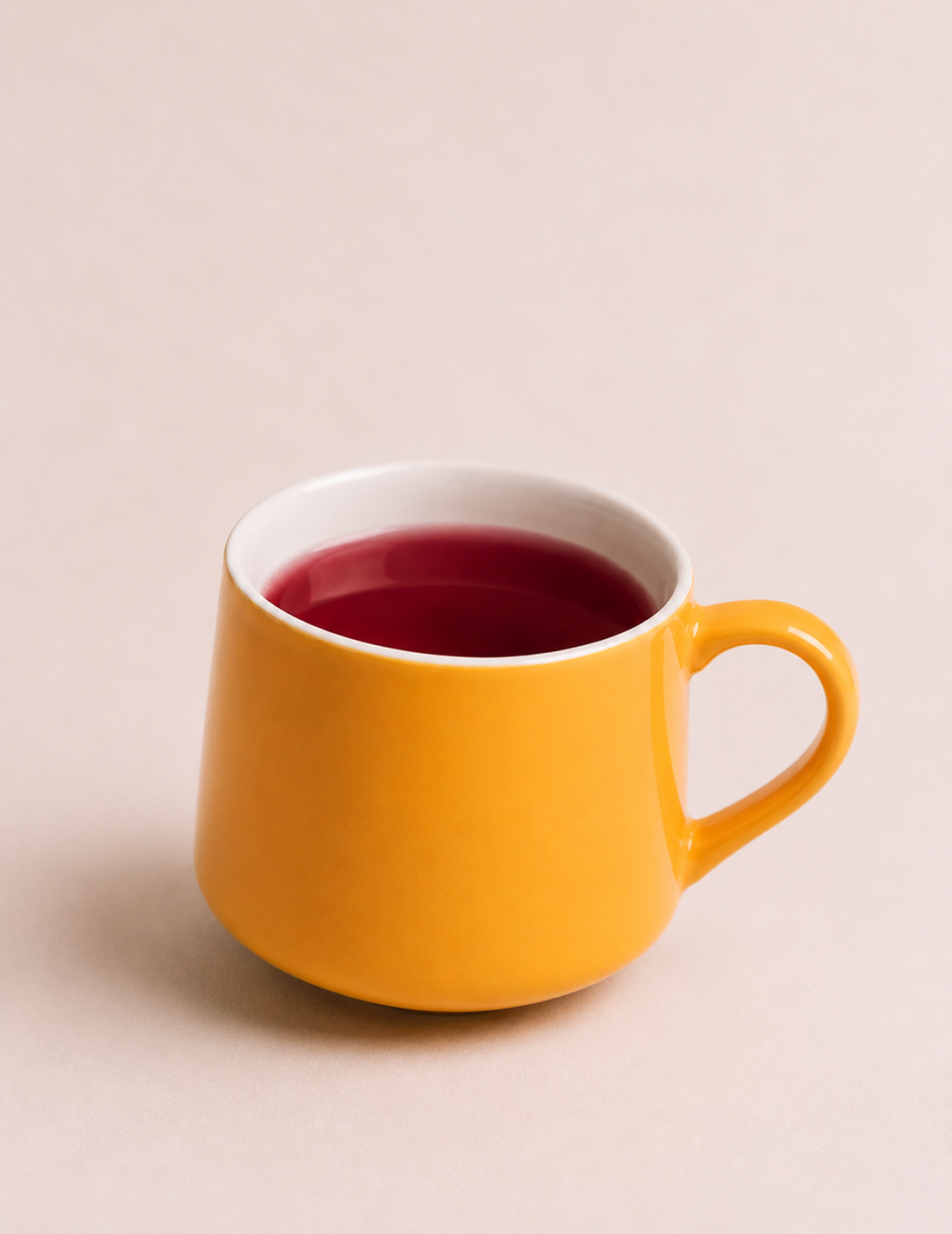 Yellow mug filled with red liquid, placed on a light beige background.