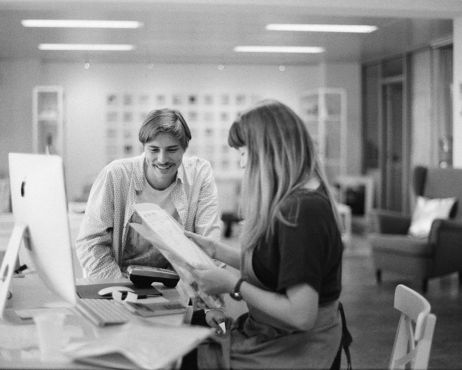 A man and a woman smiling and looking at a document in a modern office or workspace.
