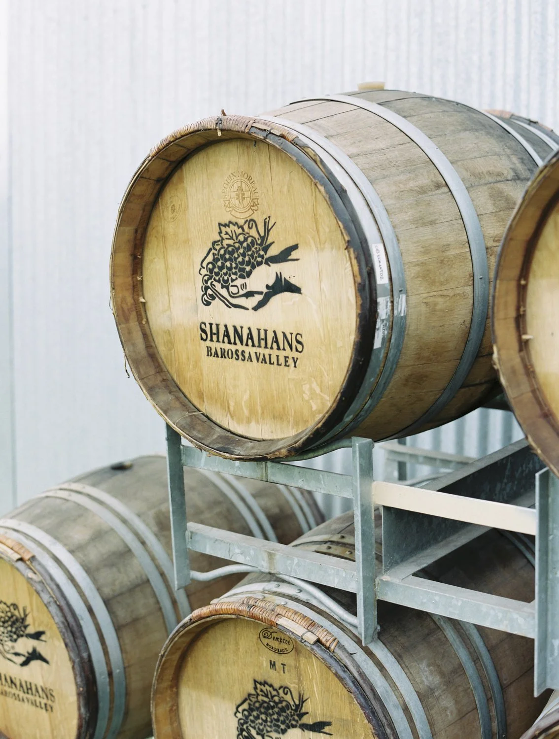 Several wooden wine barrels on a metal rack, with one barrel displaying the logo of Shanahans Barossa Valley.