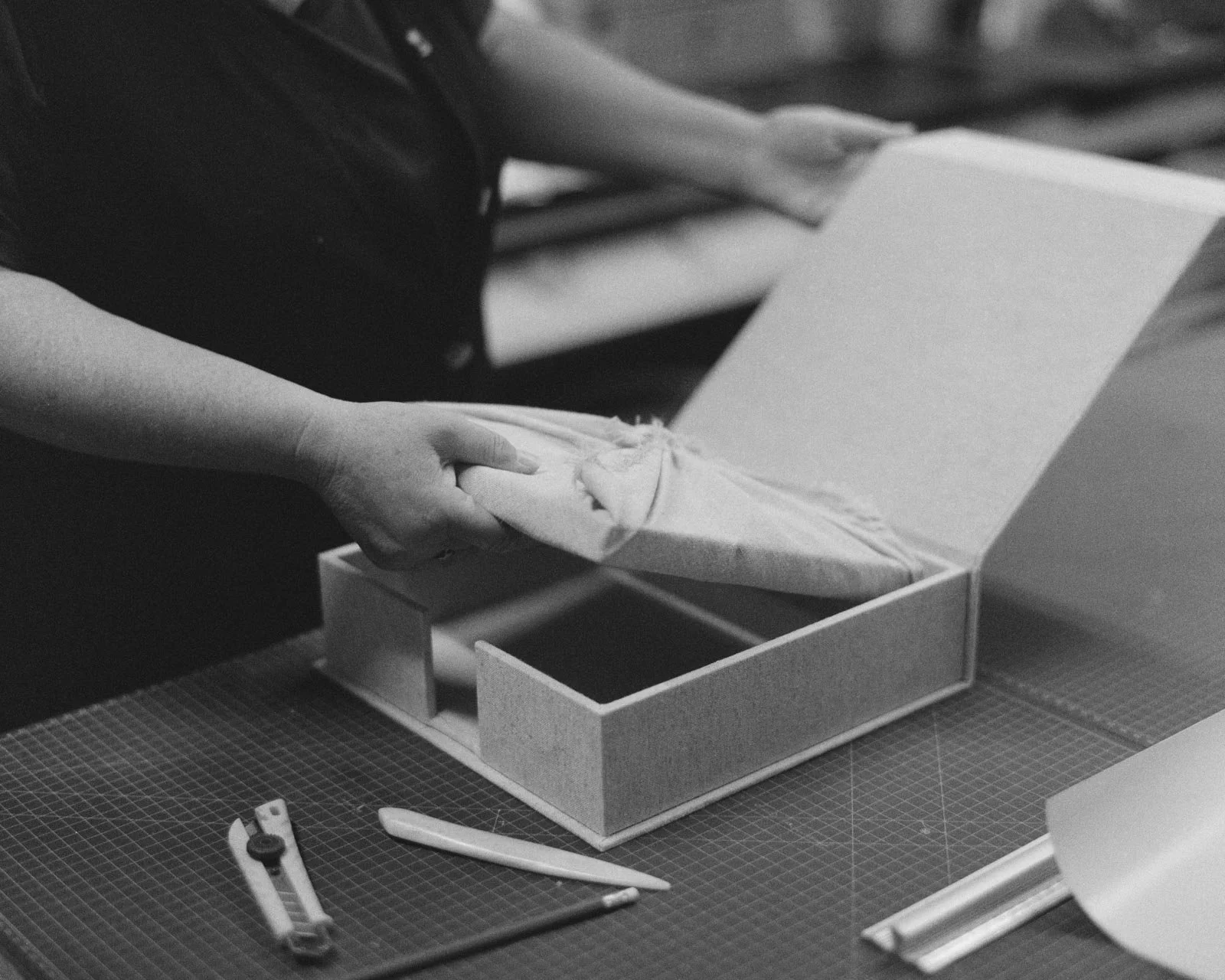 Person wrapping a gift box with tissue paper on a work table.