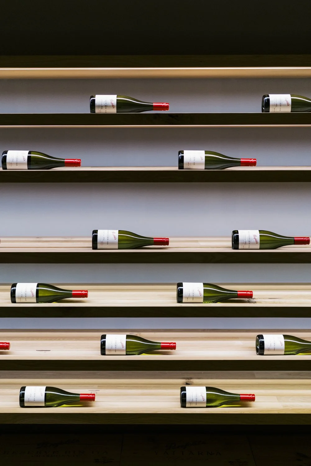 Rows of wine bottles placed horizontally on wooden shelves against a wall.
