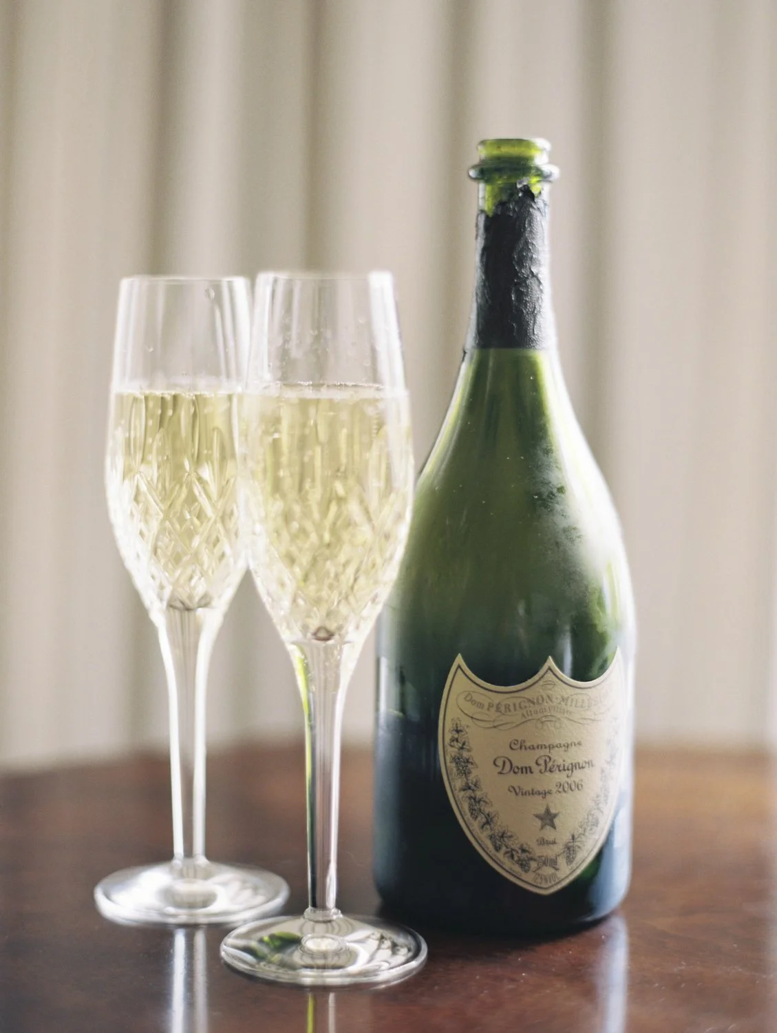 A bottle of Dom Pérignon champagne and two filled champagne flutes on a wooden surface.