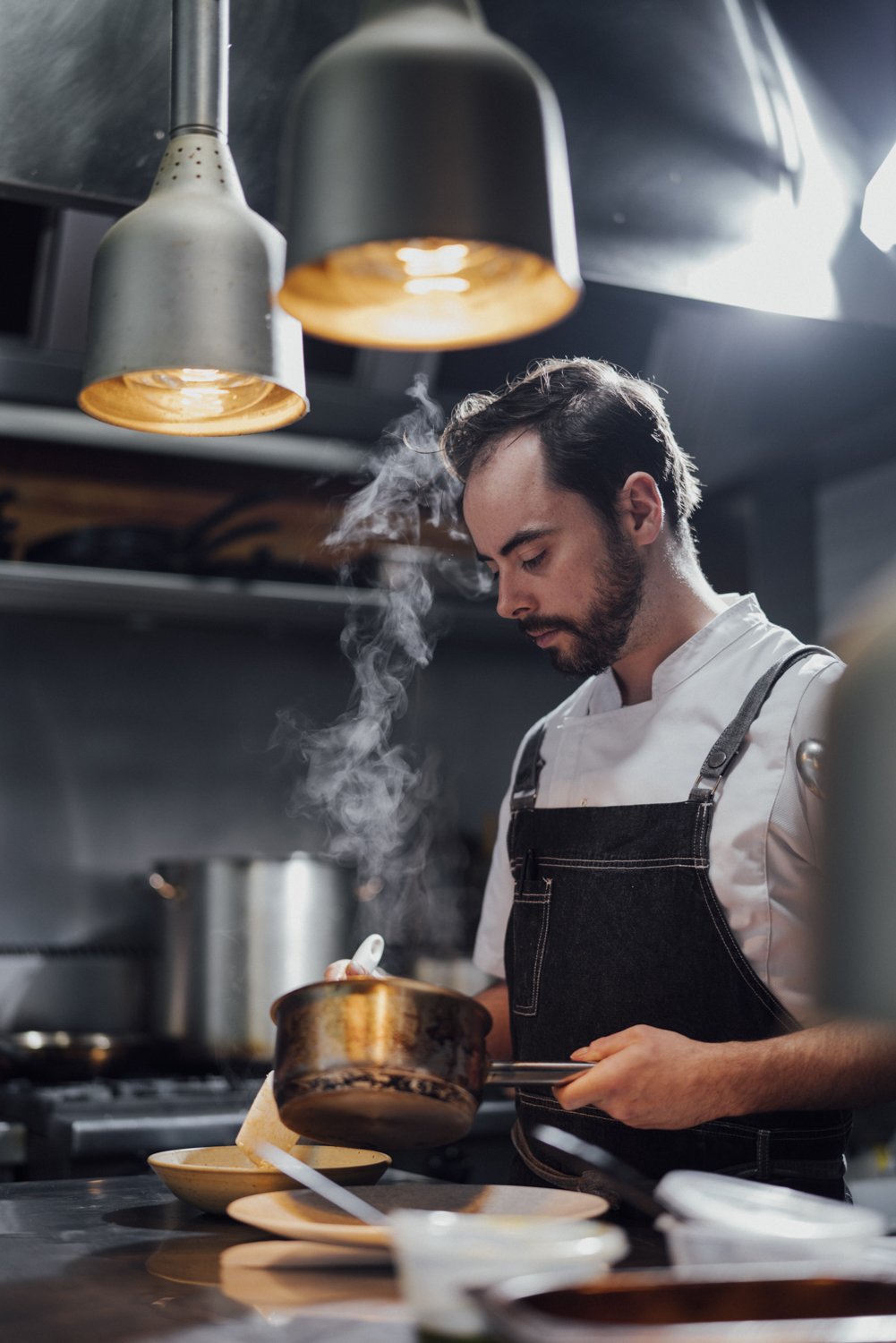 Chef cooking in a professional kitchen with steam rising from a saucepan.