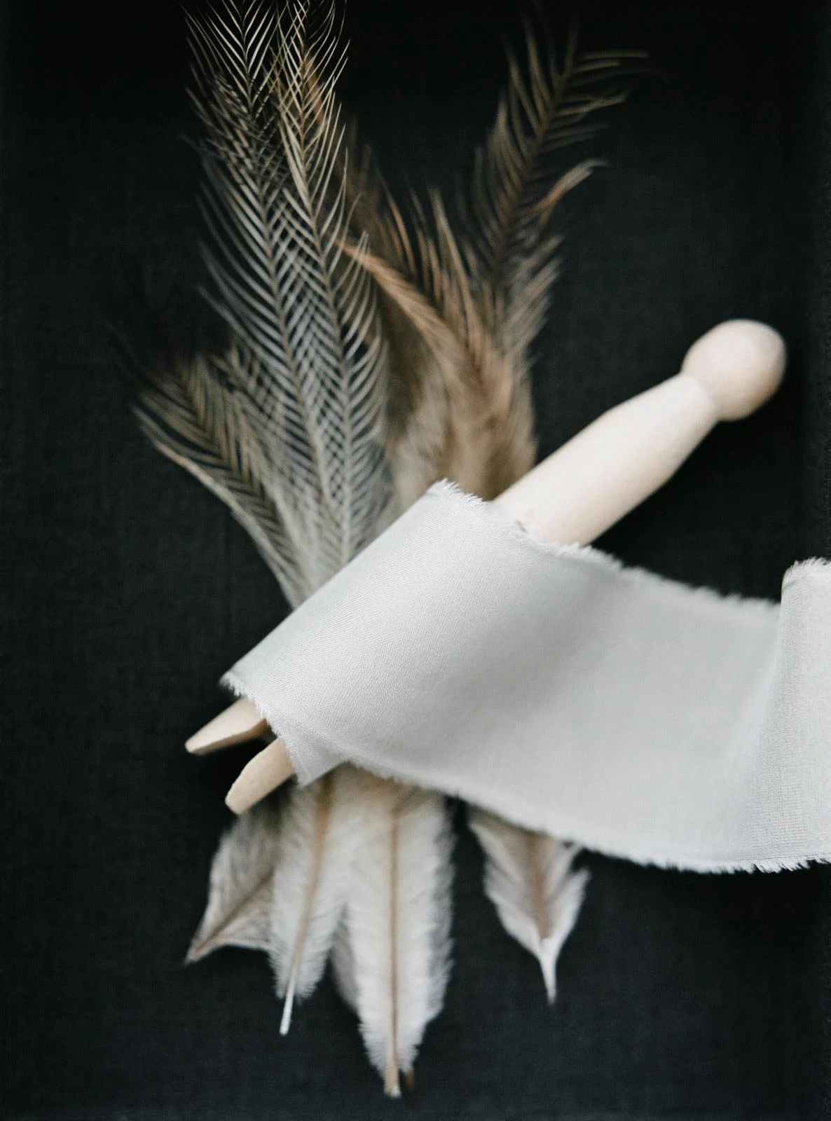 Feathers and wooden dowsing rod wrapped in white fabric on a black background.