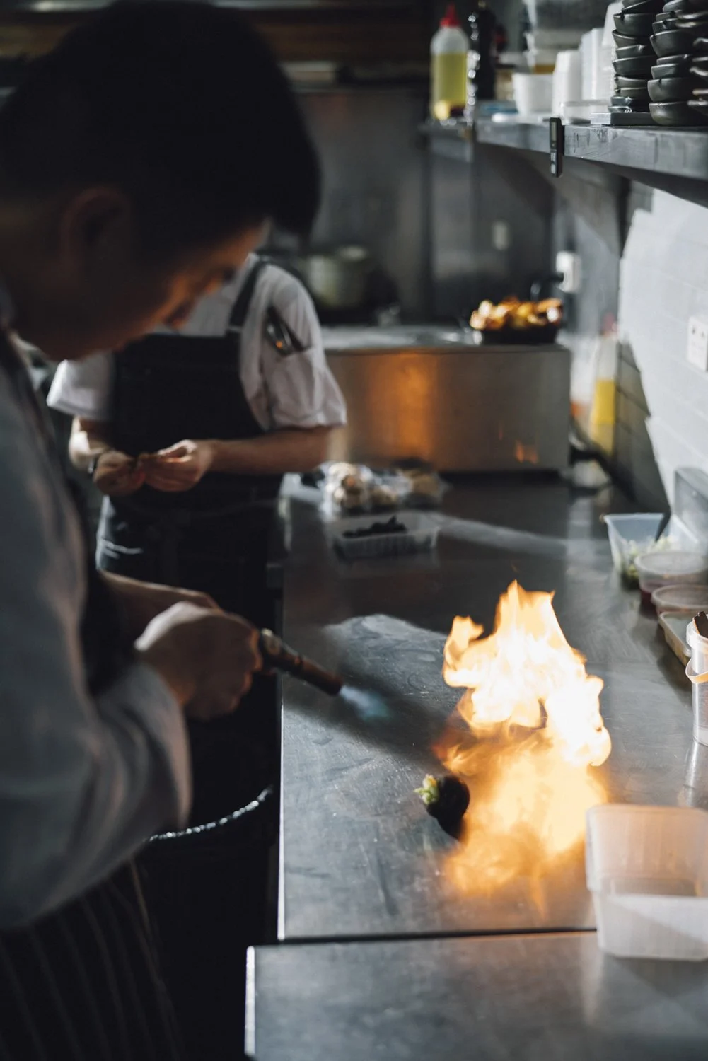 Chef igniting a flame on a dish in a professional kitchen.