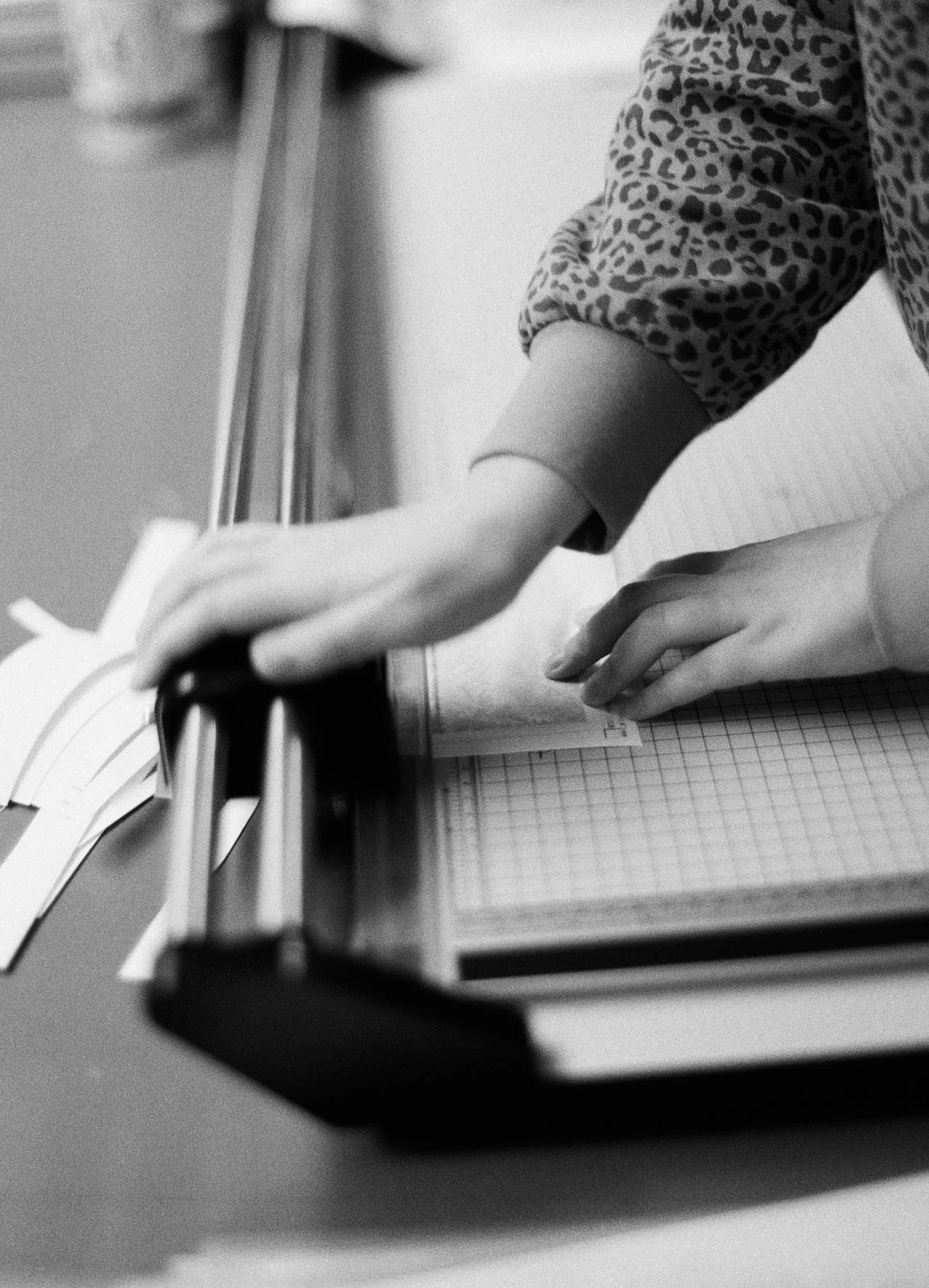 Black and white photo of a person using a hole puncher to punch holes in a piece of paper on a desk.