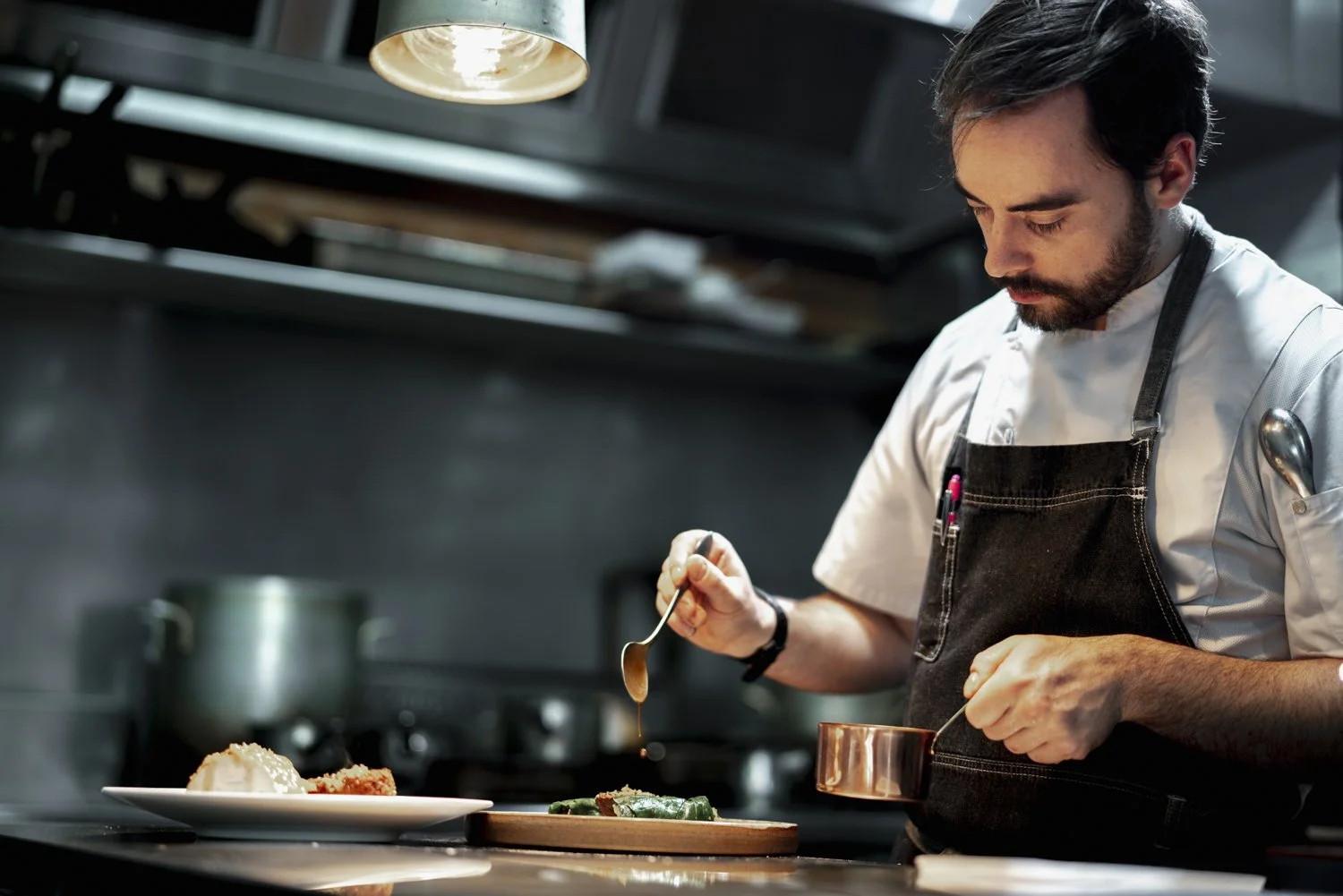 Chef garnishing a plated dish in a professional kitchen