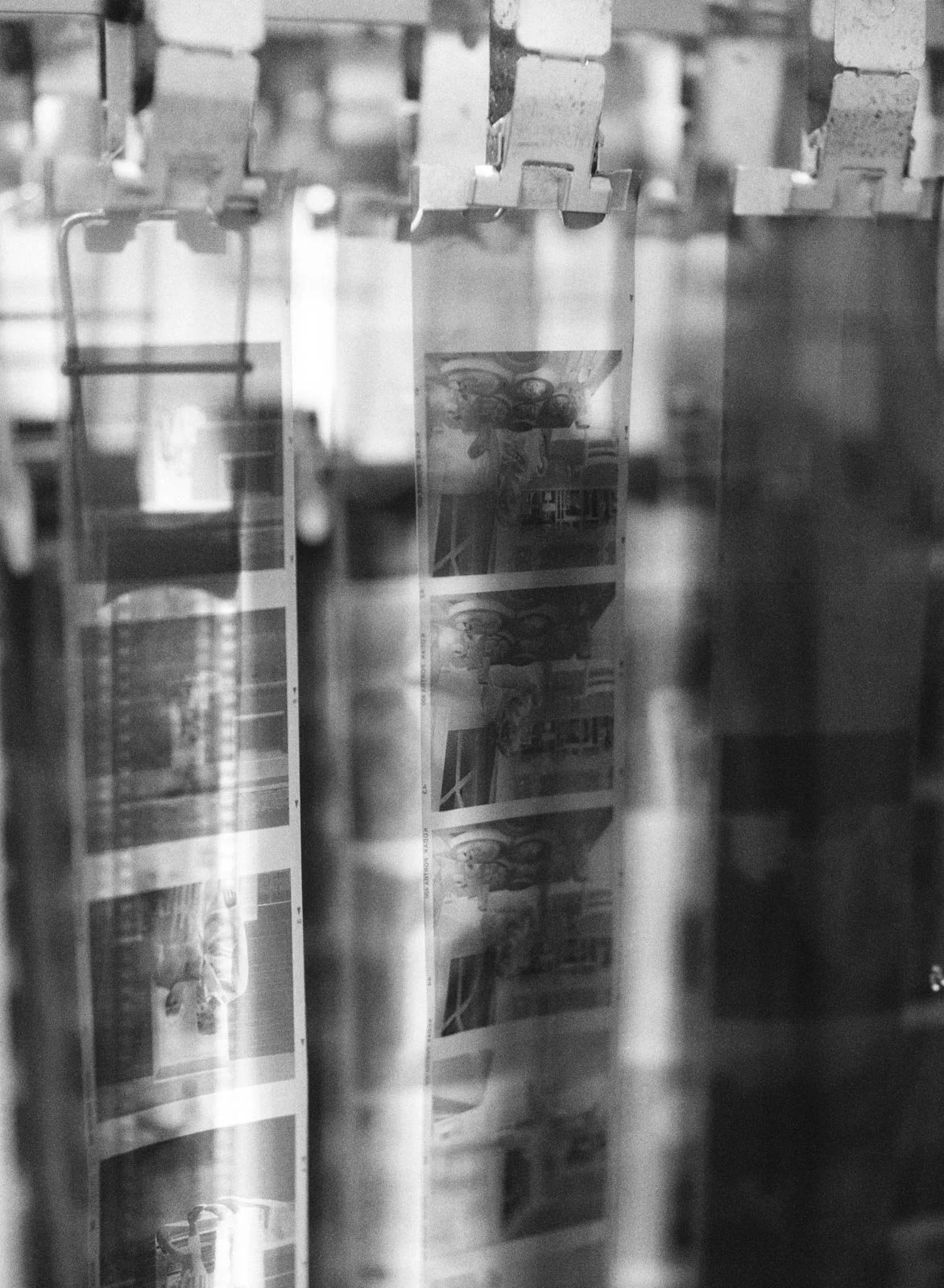Photograph of photographic contact sheets with images being developed, seen through a glass or plastic covering, in black and white.