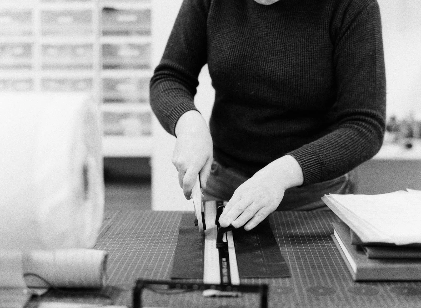 Person using a paper trimmer to cut paper on a desk with stacks of papers and a grid cutting mat.
