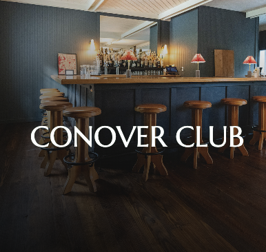Bar area with wooden stools and a large mirror behind the counter, labeled 'Conover Club' in white text.