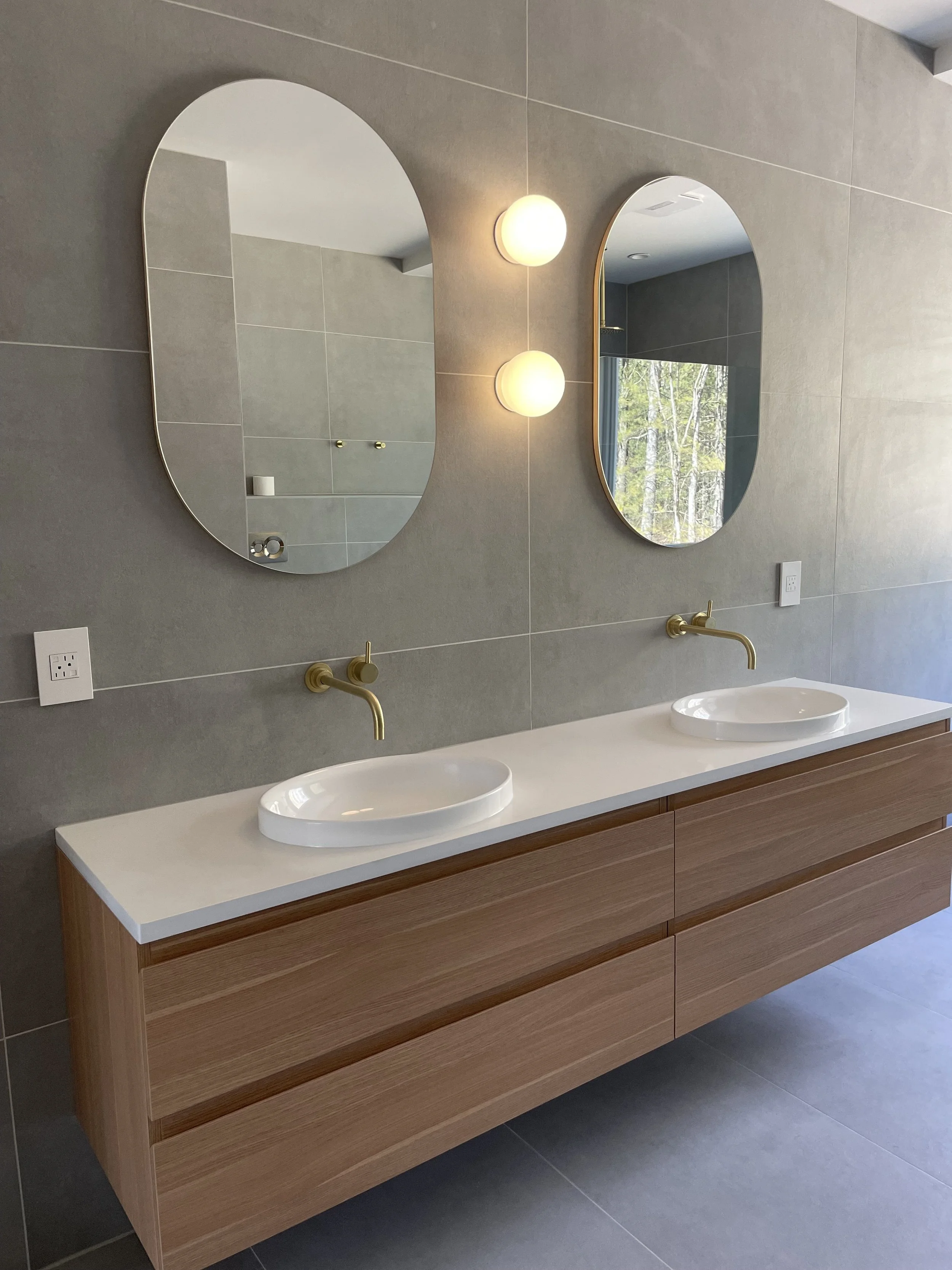 Modern bathroom with double vanity featuring two oval mirrors, two wall-mounted faucets, and a wooden cabinet with six drawers.