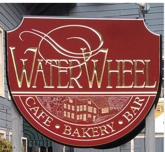 Red and gold sign for Waterwheel Cafe Bakery Bar, featuring a drawing of a waterwheel and a building.