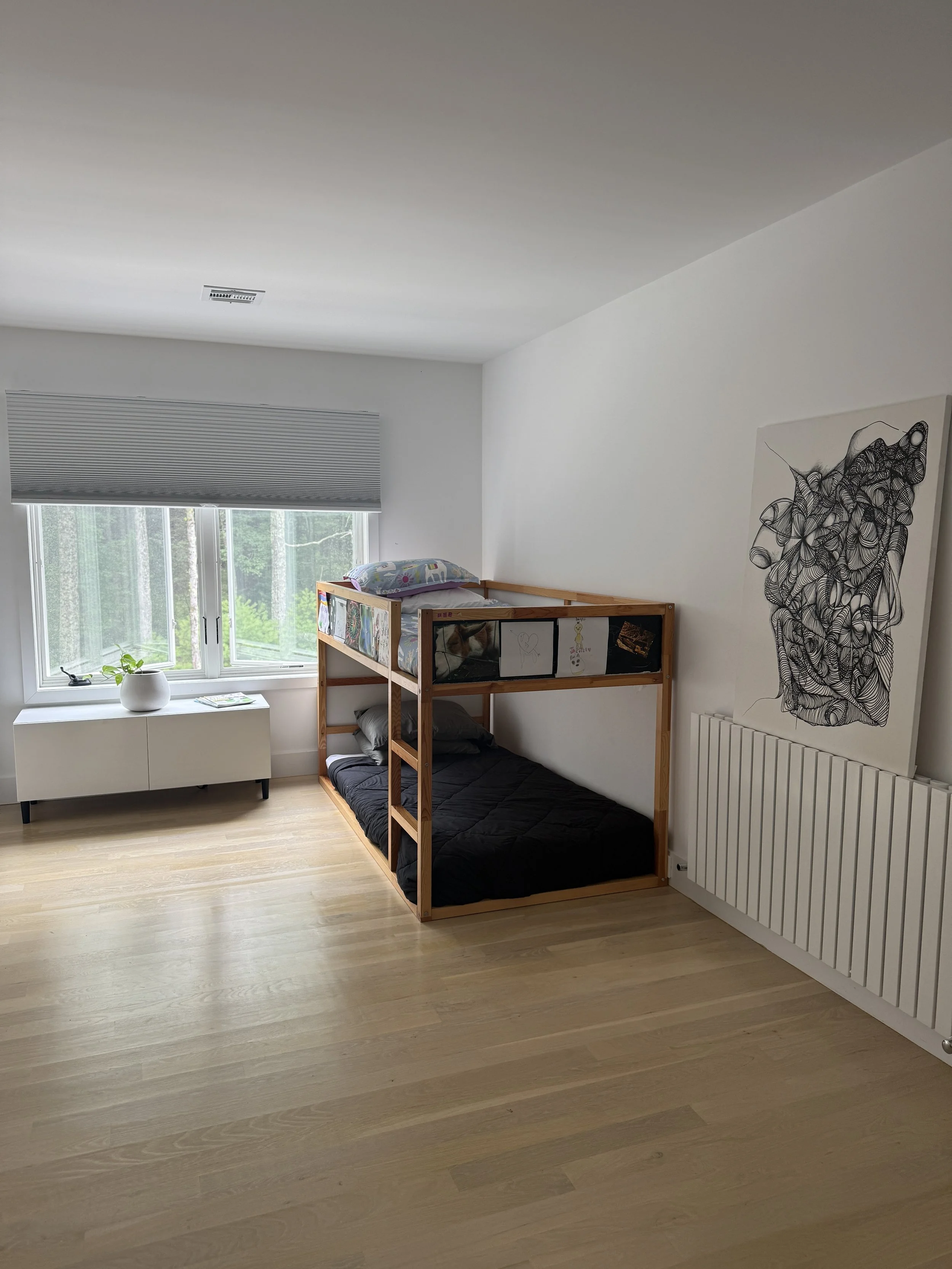 A minimalist bedroom with a bunk bed, a window with a gray blind, a white cabinet, and a piece of black and white abstract art on the wall.