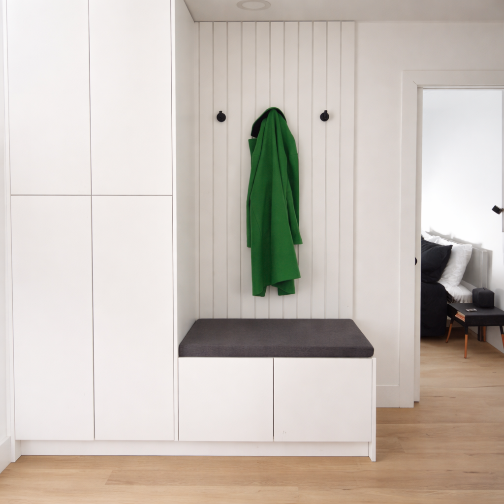 A modern white entryway with a built-in cabinet and a cushioned bench, featuring black hooks for your coats and shoes ! 
