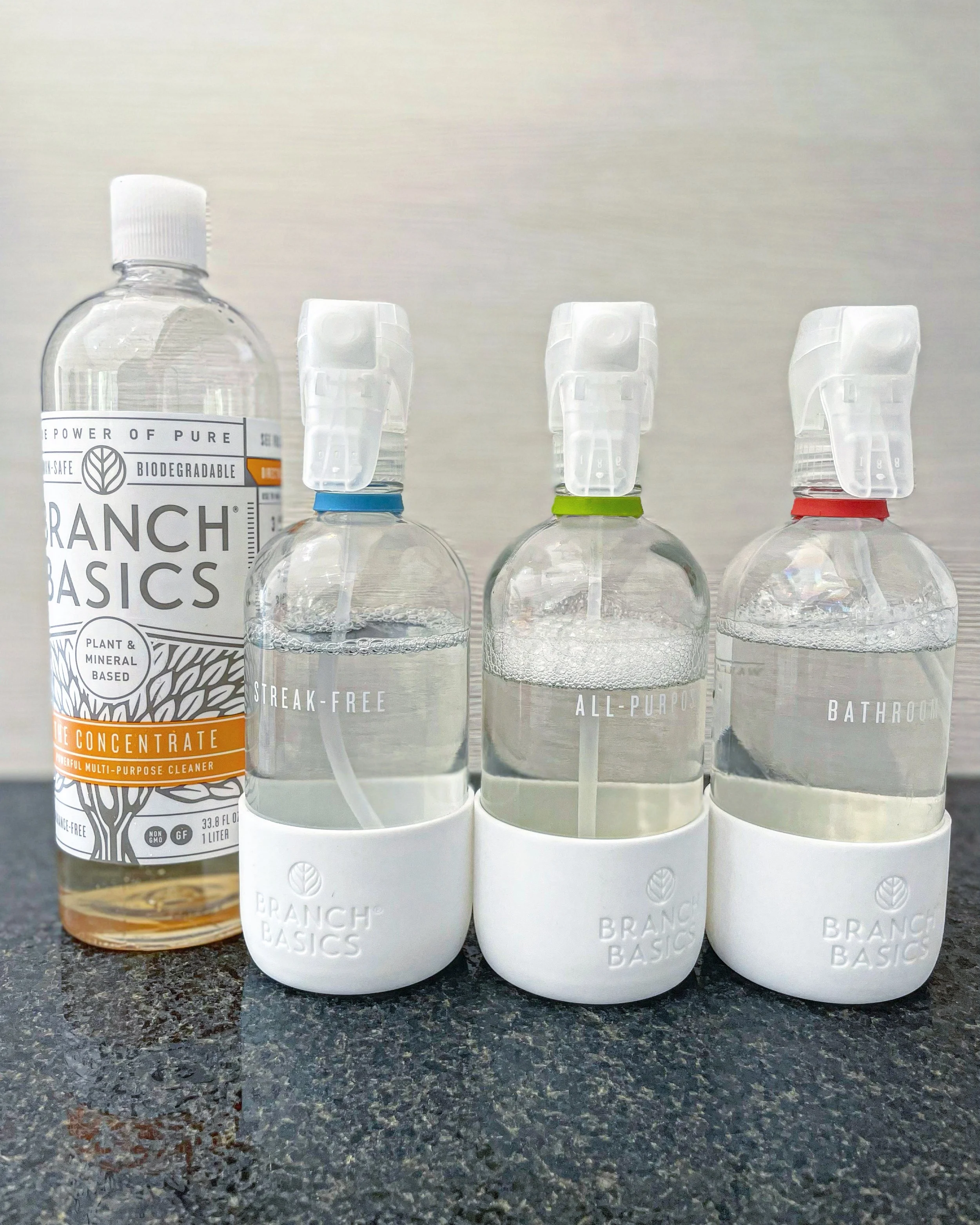 Three spray bottles filled with clear liquid, labeled 'Streak-Free,' 'All-Purpose,' and 'Bathroom,' with one larger bottle of Ranch Basics multi-purpose cleaner next to them.
