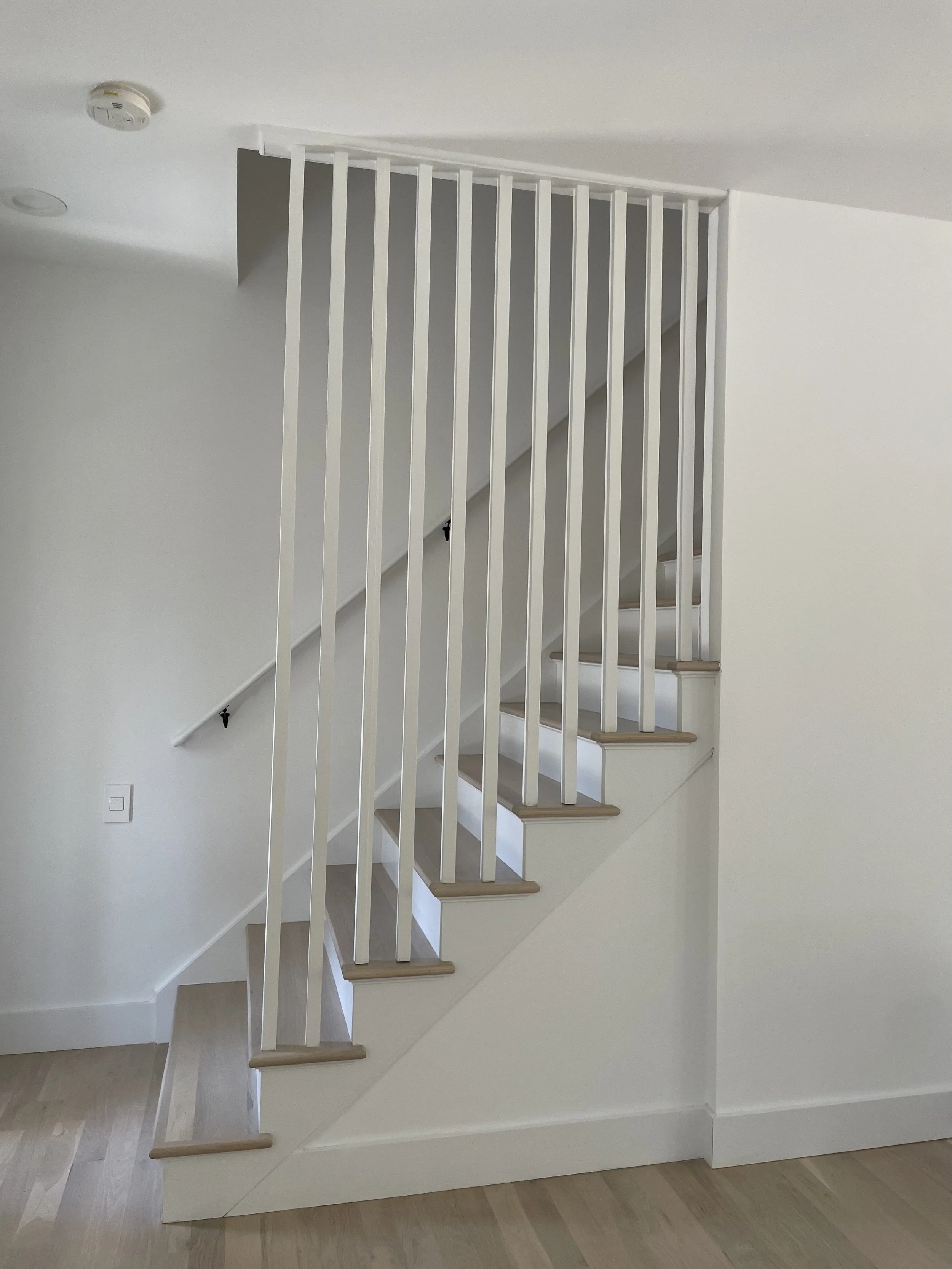 Modern interior staircase with wooden steps and white vertical railing in a bright, minimalistic home.