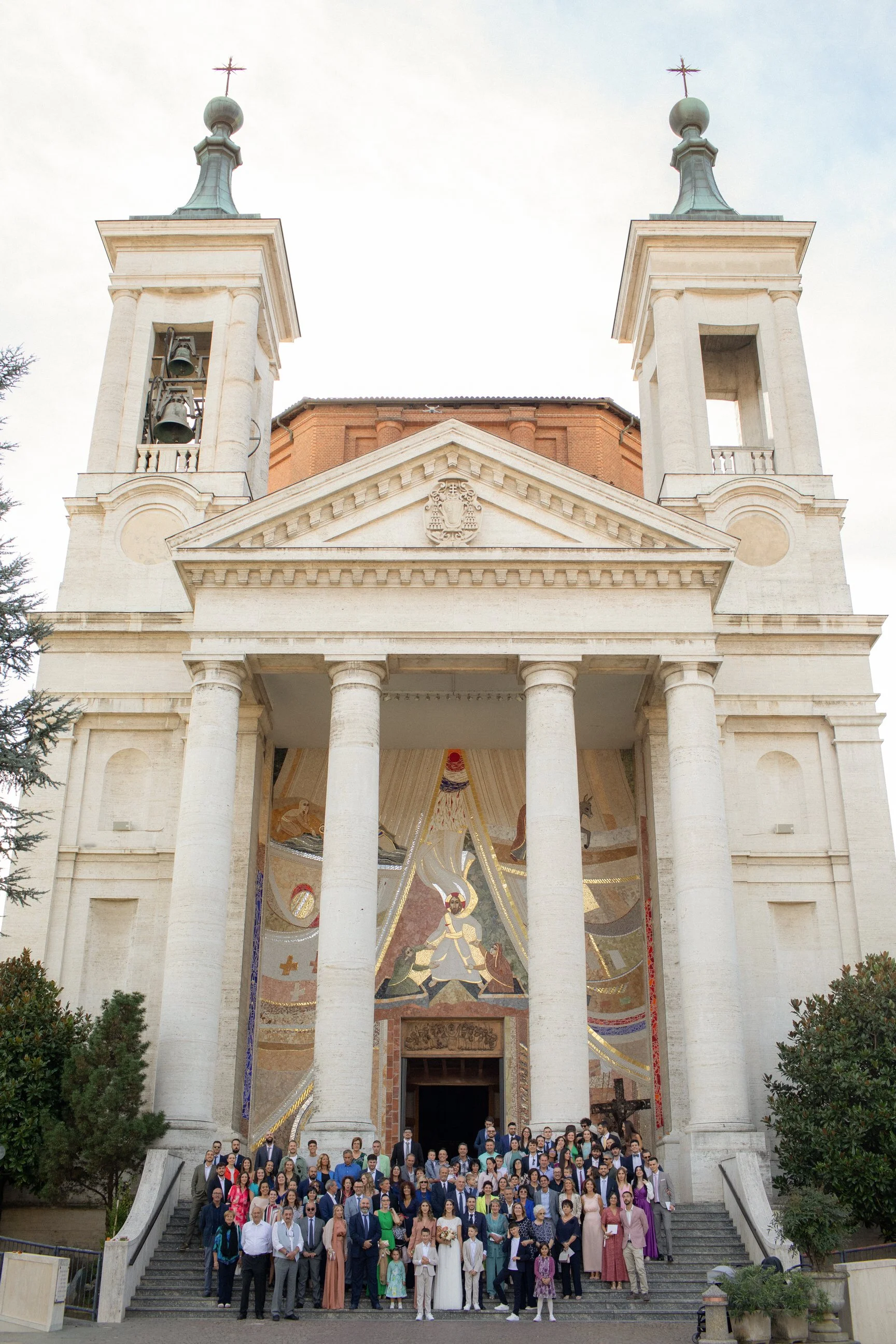Gruppo di persone davanti a una chiesa con due torri e un mosaico sopra l'ingresso.
