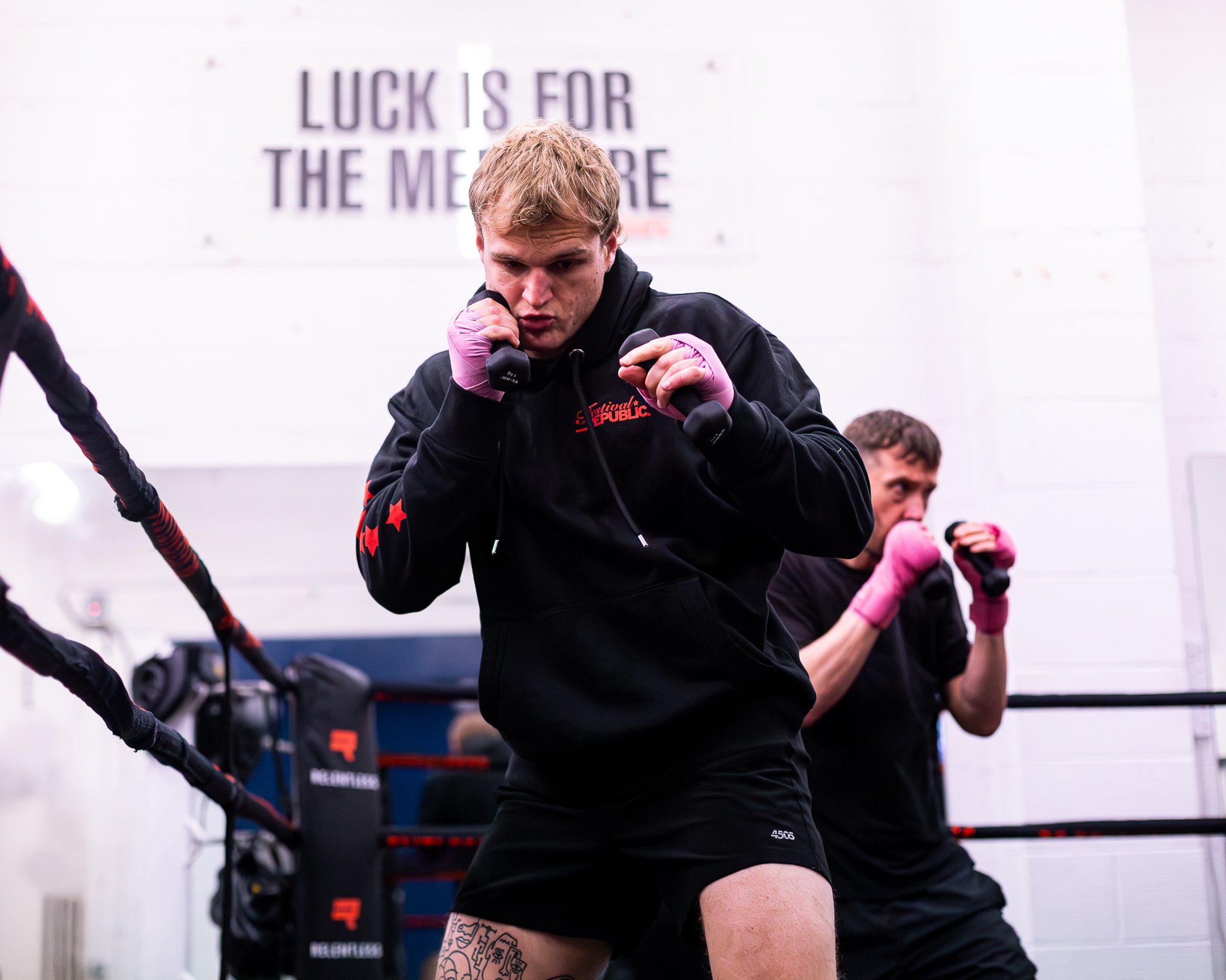 Boxers practicing in a boxing gym with a coach and kickboxers sparring inside a boxing ring.