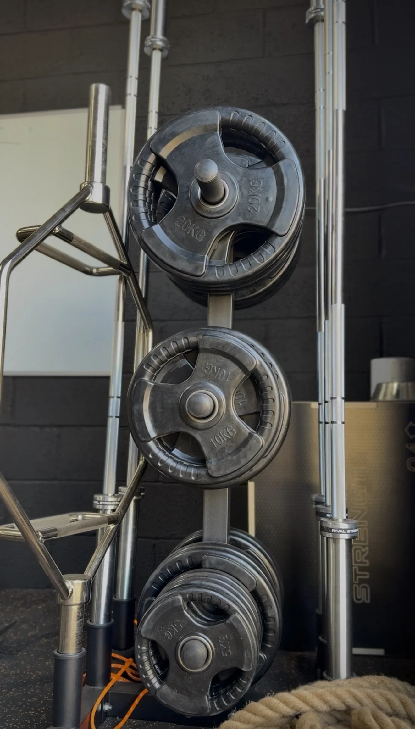 A vertical rack holding four adjustable weight plates, each labeled 20KG and 10KG, with metal frame and black background.