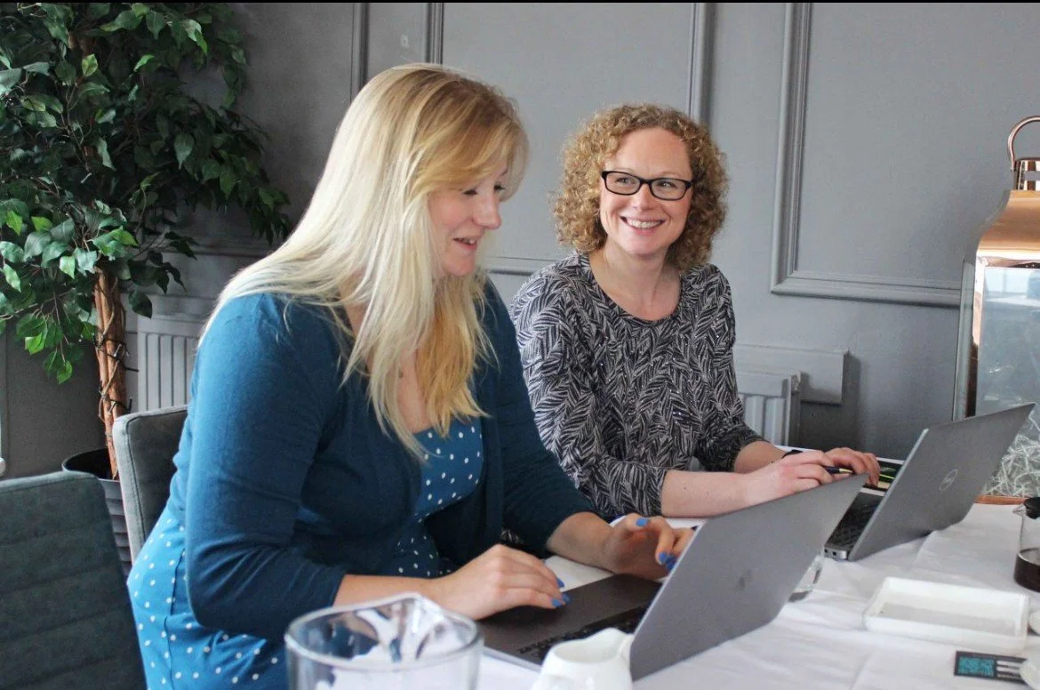 Two women sitting at a table with laptops for Expert Bid Writing Service and Bid Support