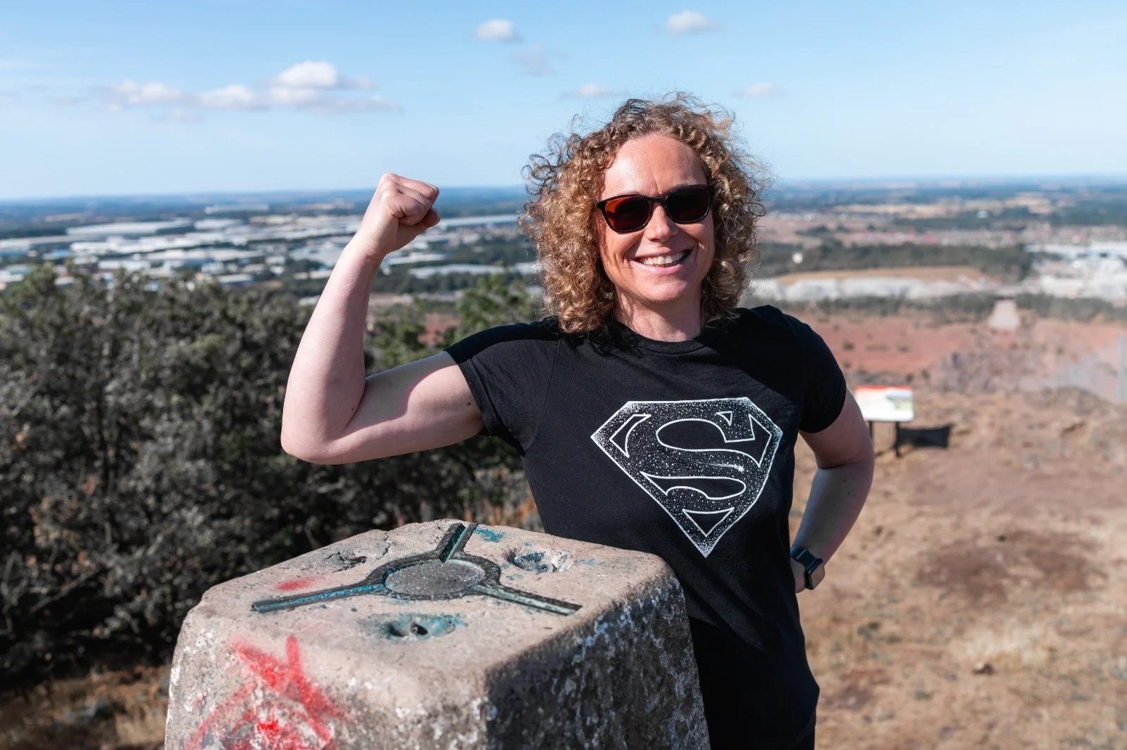 Joanne Tryner, founder of Wordsmith Projects, tensing her biceps while wearing a Super Girl tee shirt.