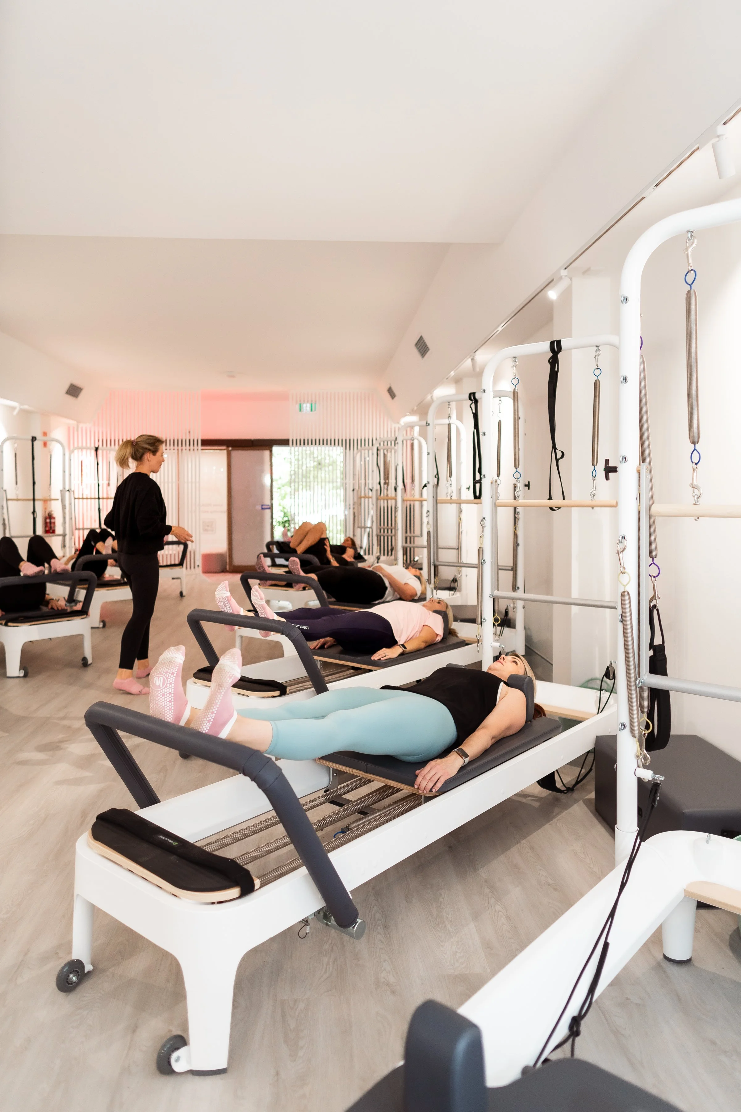 Women practicing Pilates on reformer machines in a fitness studio with instructor nearby.