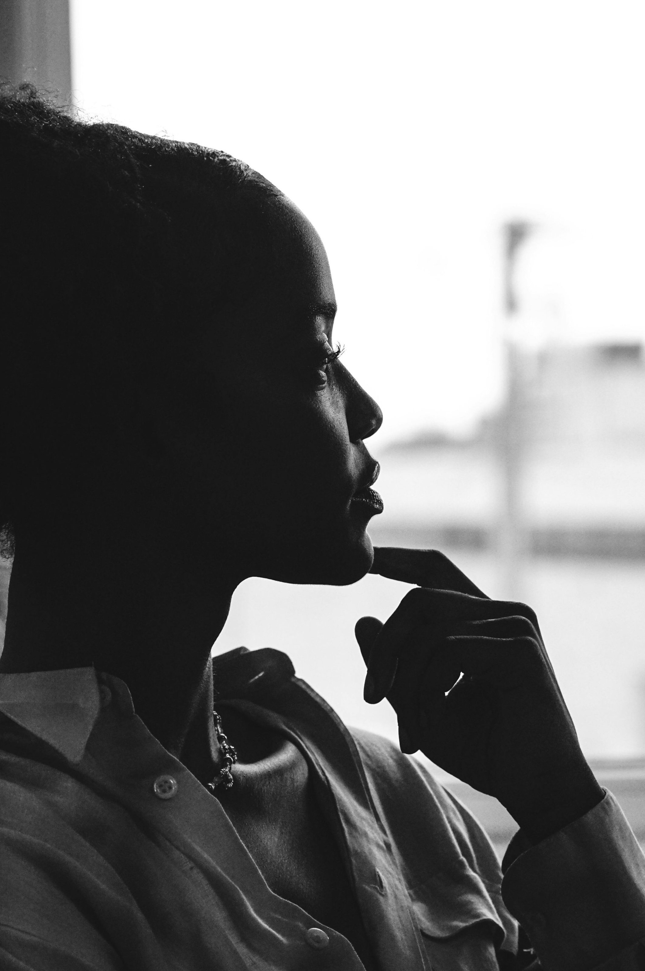 Side profile of a woman with her hand near her chin, looking thoughtfully out a window.