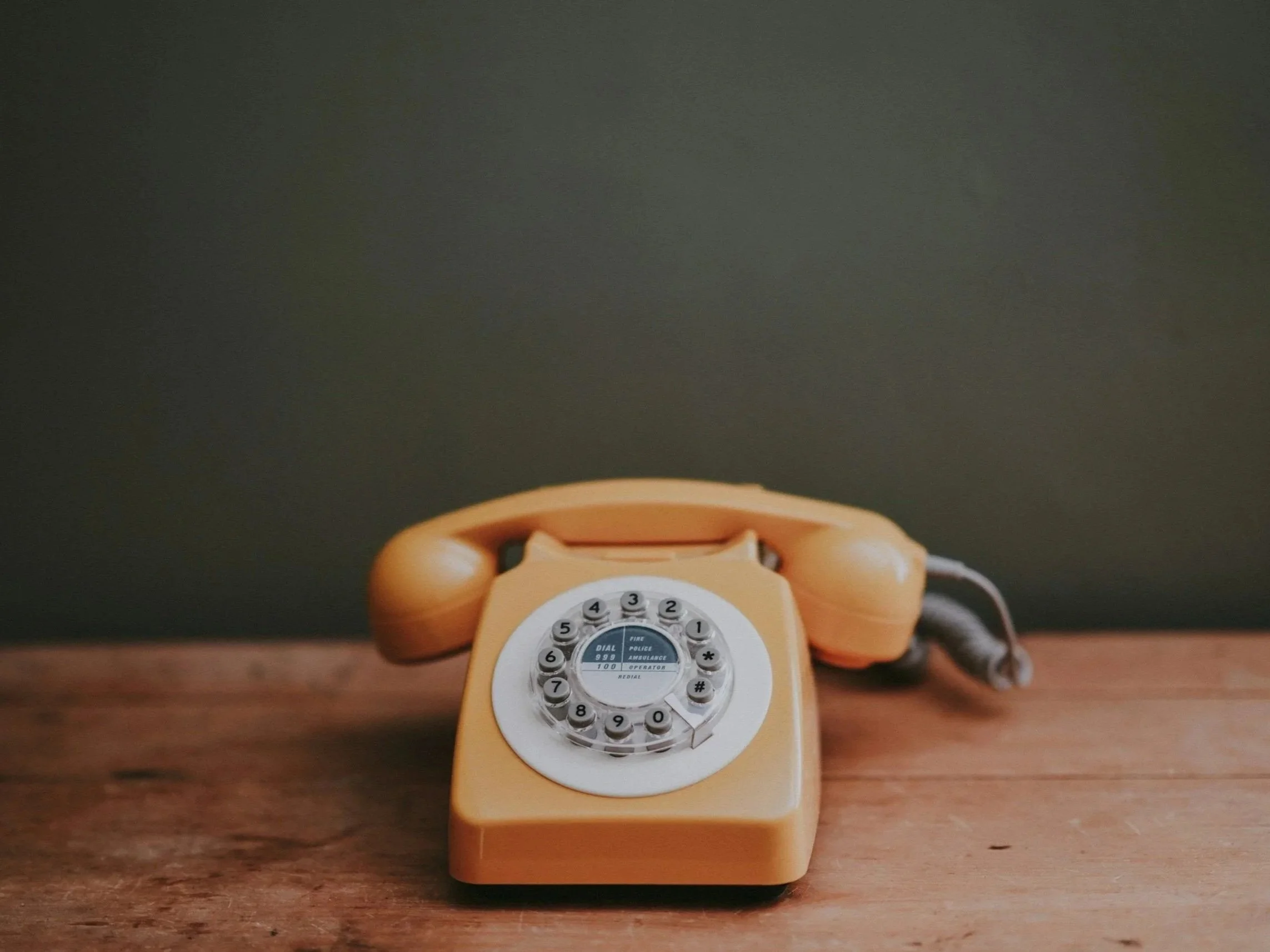 Orange rotary dial telephone on a wooden surface against a dark wall.